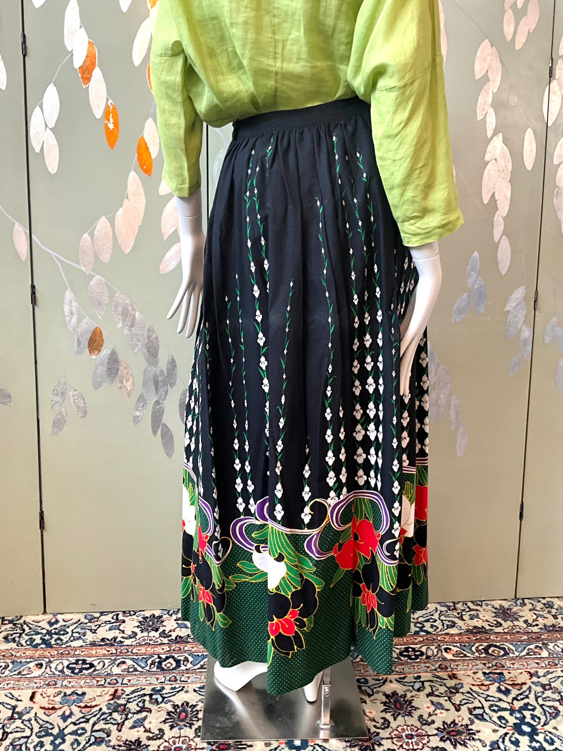 Mannequin wearing a green top and black floral skirt against a decorative wall.