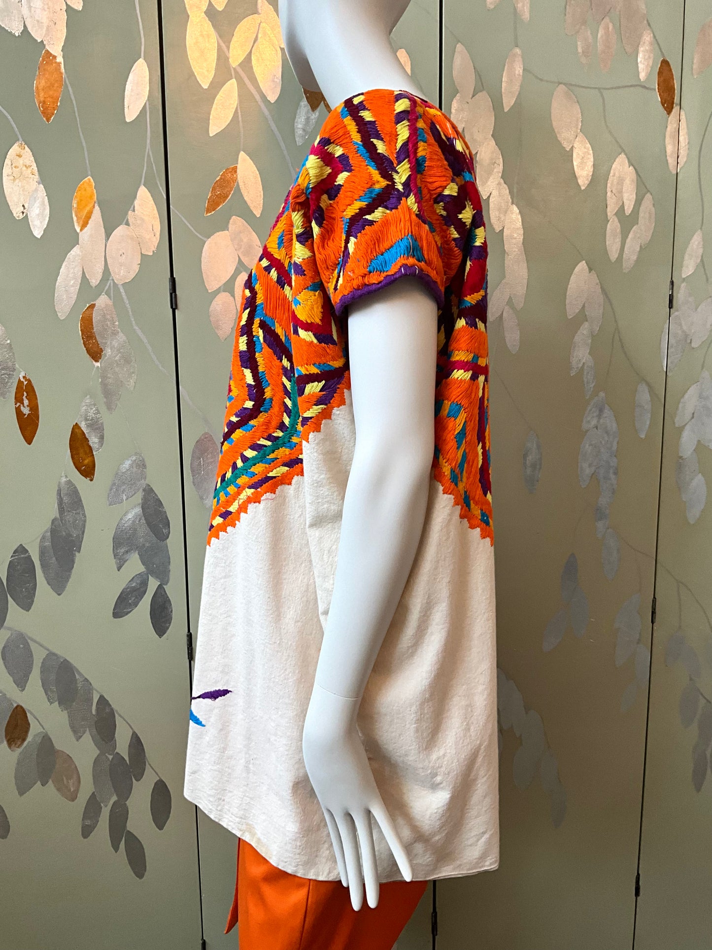 Mannequin wearing a colorful top and orange skirt with a patterned background