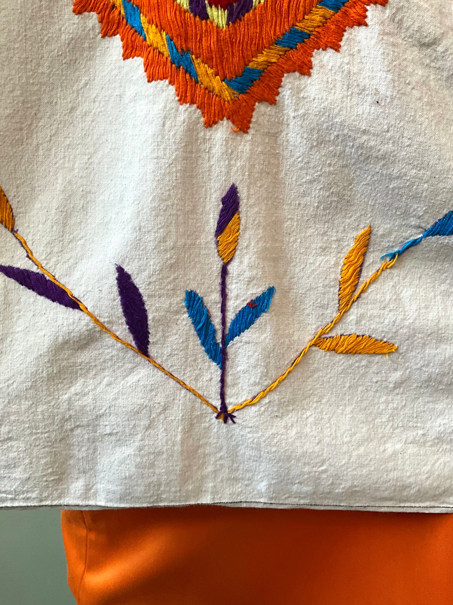 Embroidered design on a white fabric with orange, blue, and purple threads.