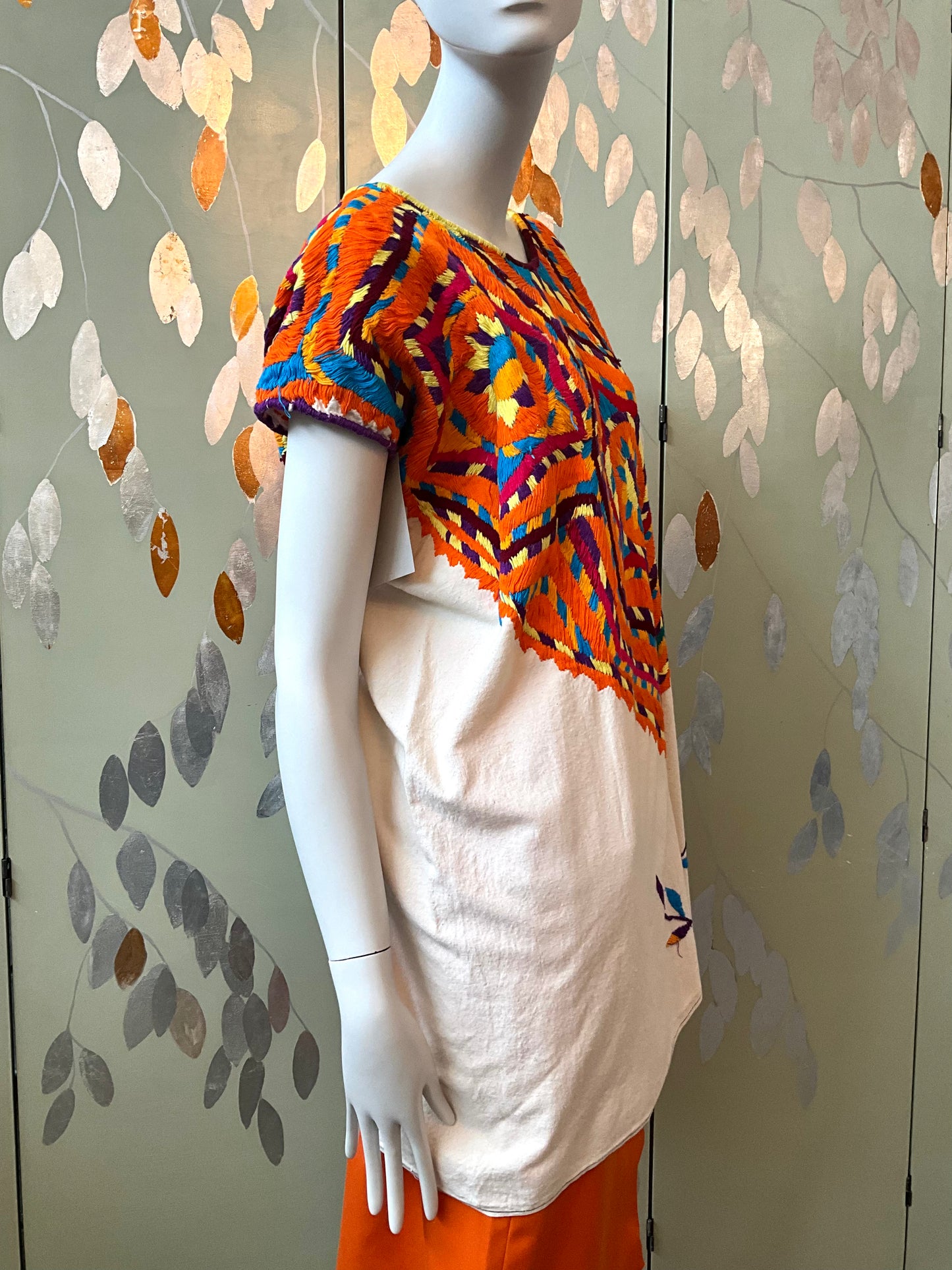 Mannequin wearing a colorful top and orange skirt against a decorative wall.