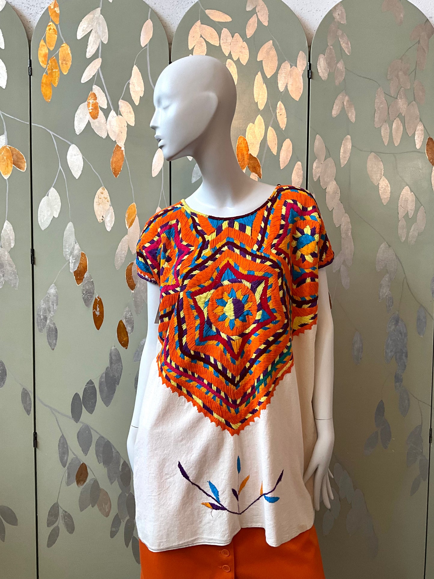 Mannequin wearing a colorful geometric-patterned top with an orange skirt against a decorative wall.
