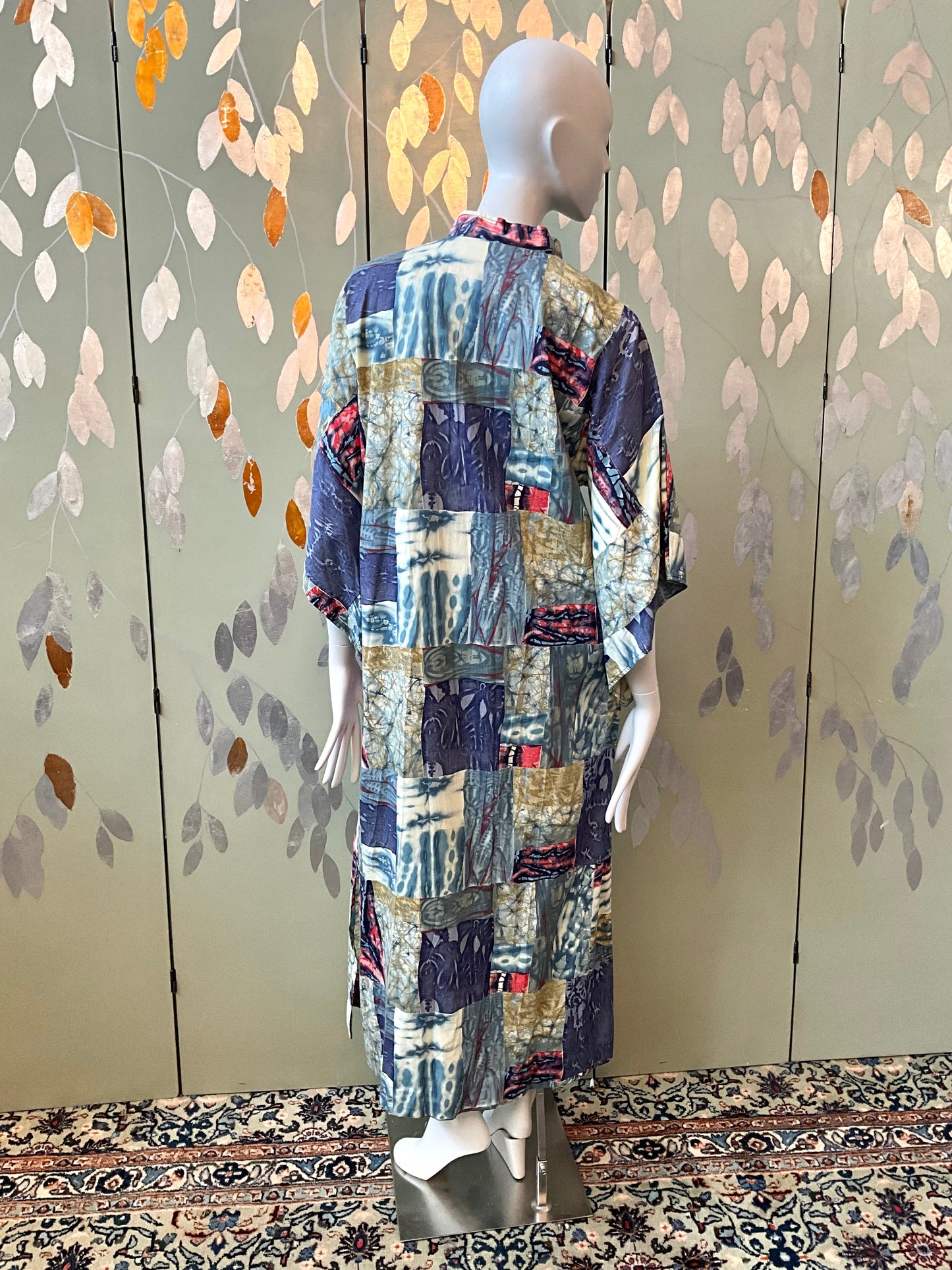 Mannequin wearing a patchwork dress against a decorative wall.