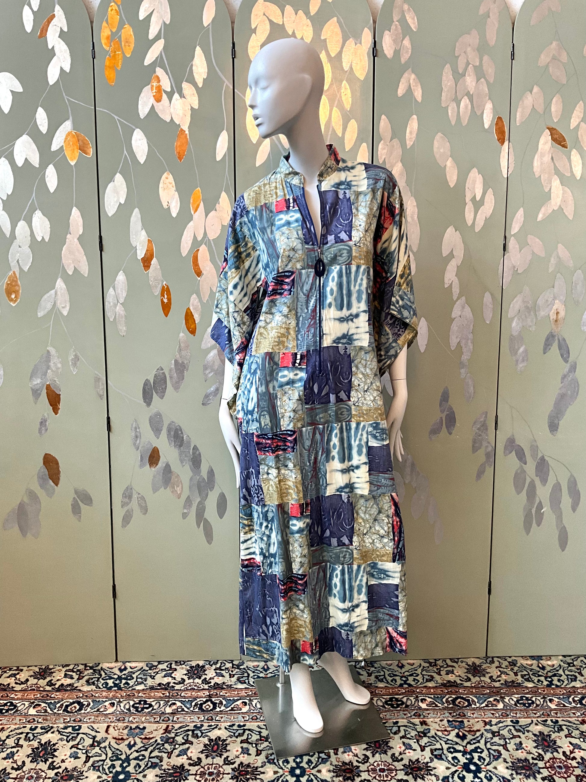 Mannequin wearing a patchwork dress against a decorative wall with leaf patterns.