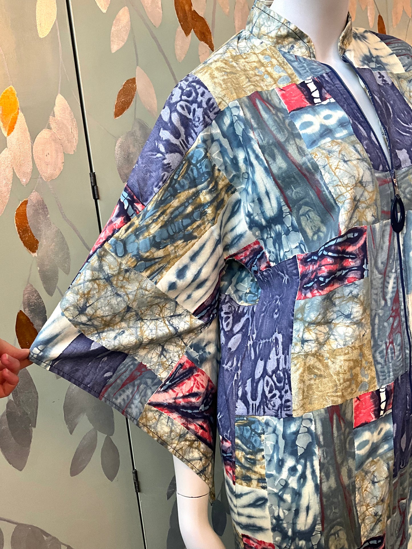 Mannequin wearing a colorful patchwork dress against a patterned wall.