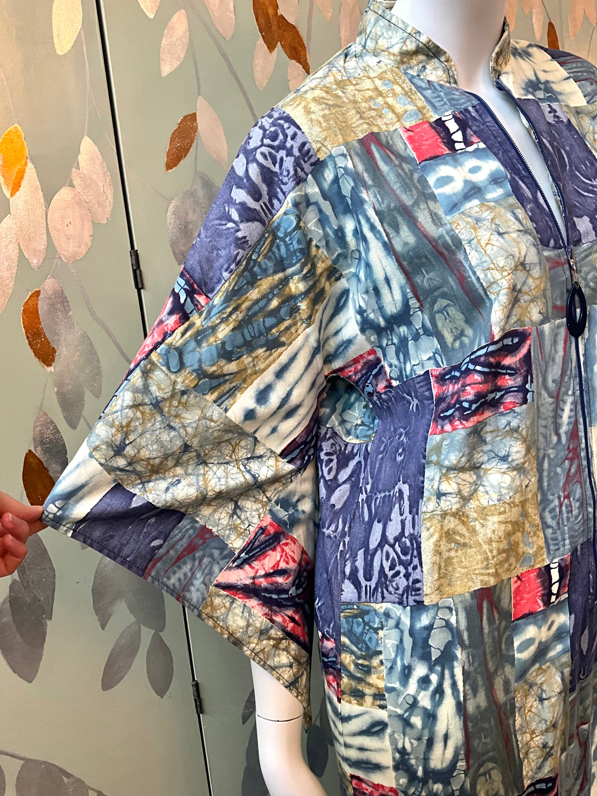 Mannequin wearing a colorful patchwork dress against a patterned wall.