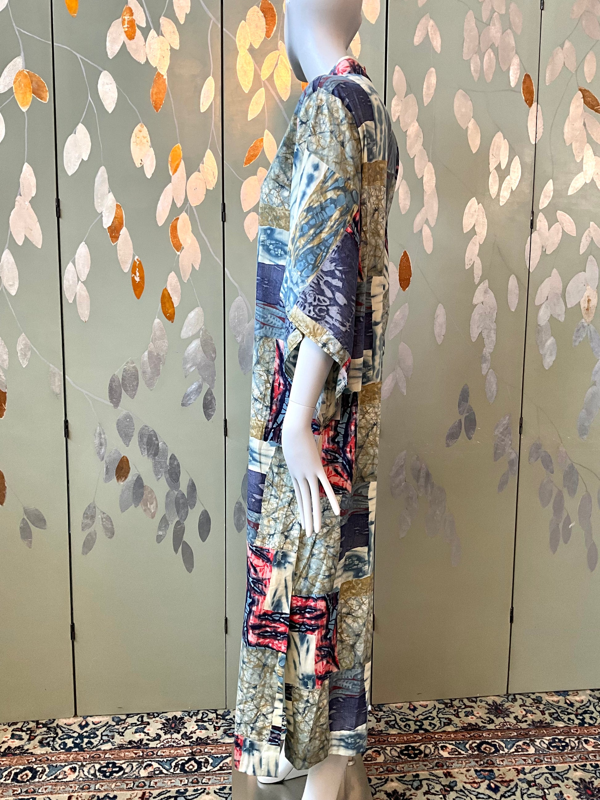 Mannequin wearing a colorful dress against a decorative wall with floral patterns.