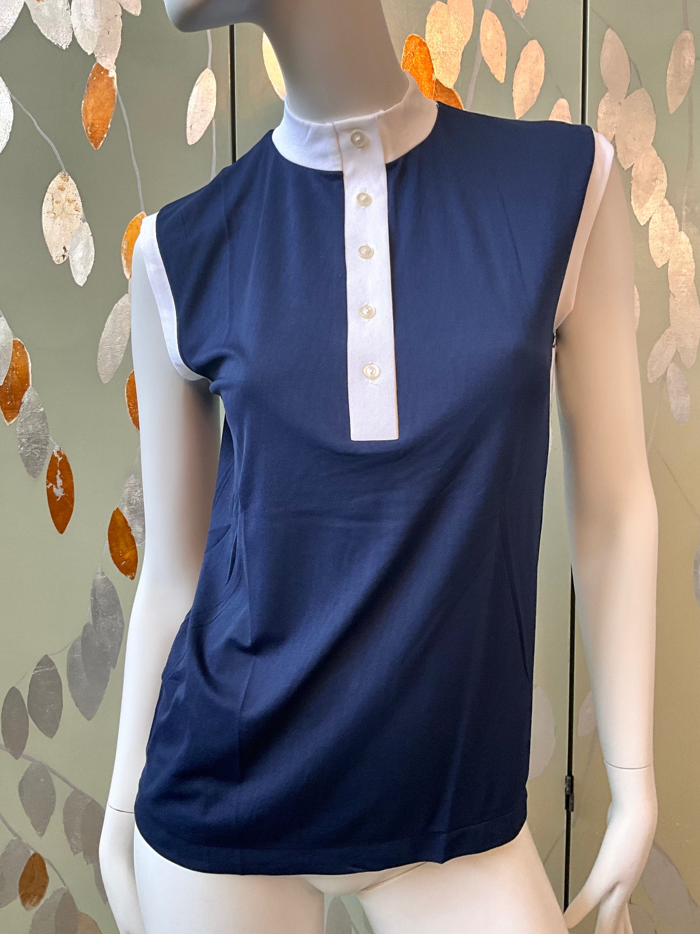 Navy blue sleeveless top with white collar on a mannequin against a leaf-patterned wall.