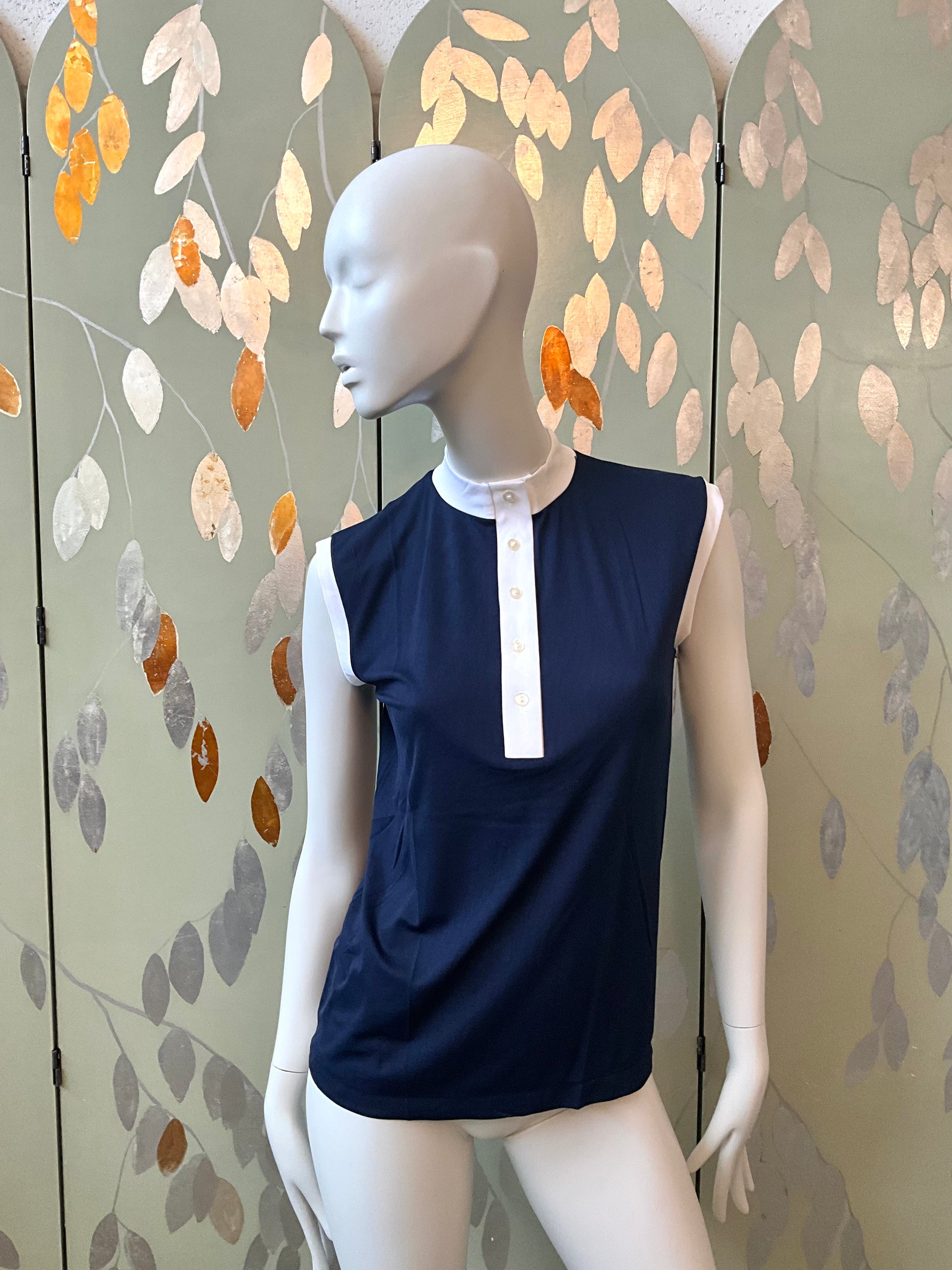 Mannequin wearing a navy blue top with a white collar against a decorative wall.