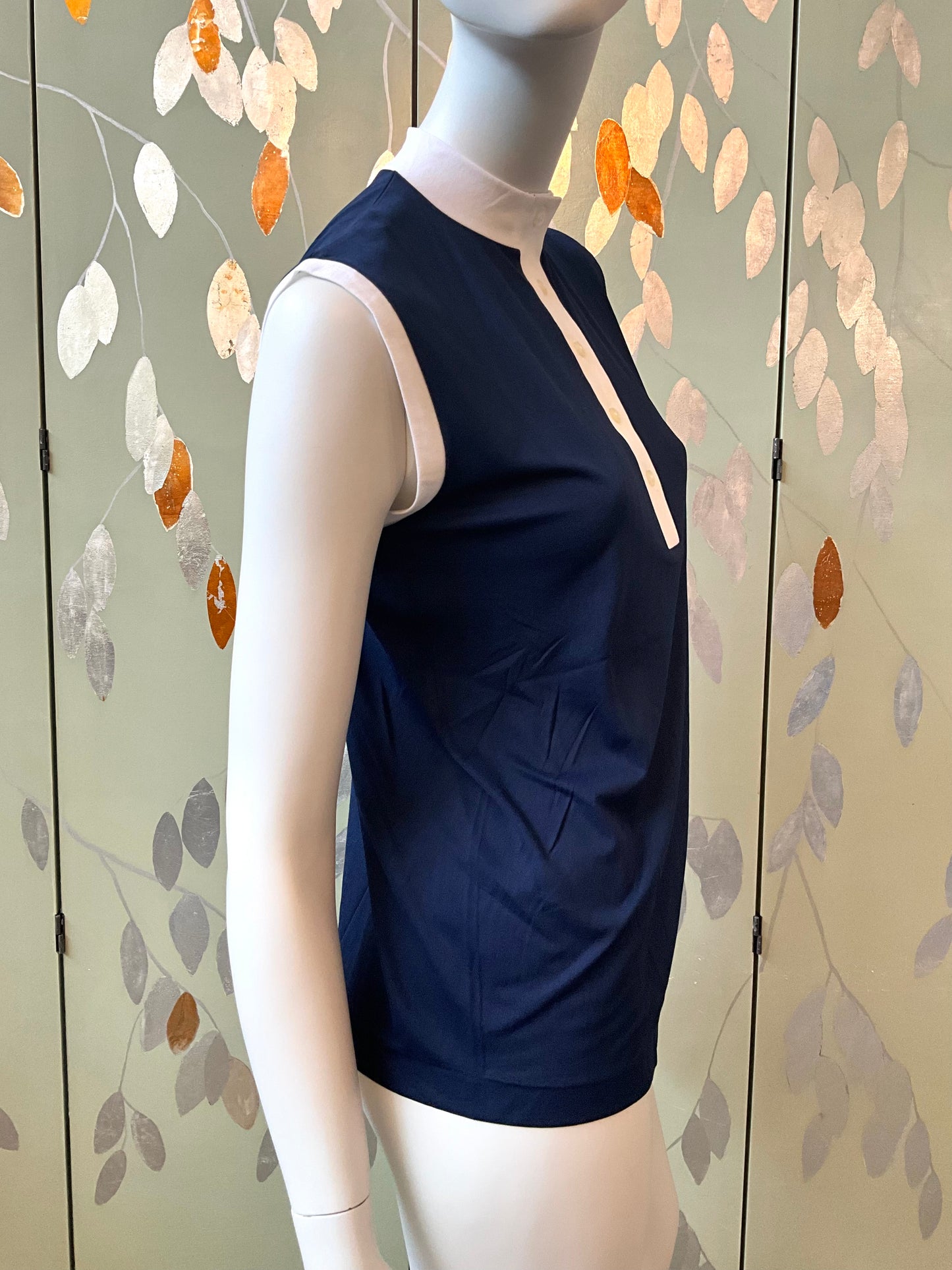 Navy sleeveless top on a mannequin against a decorative wall.