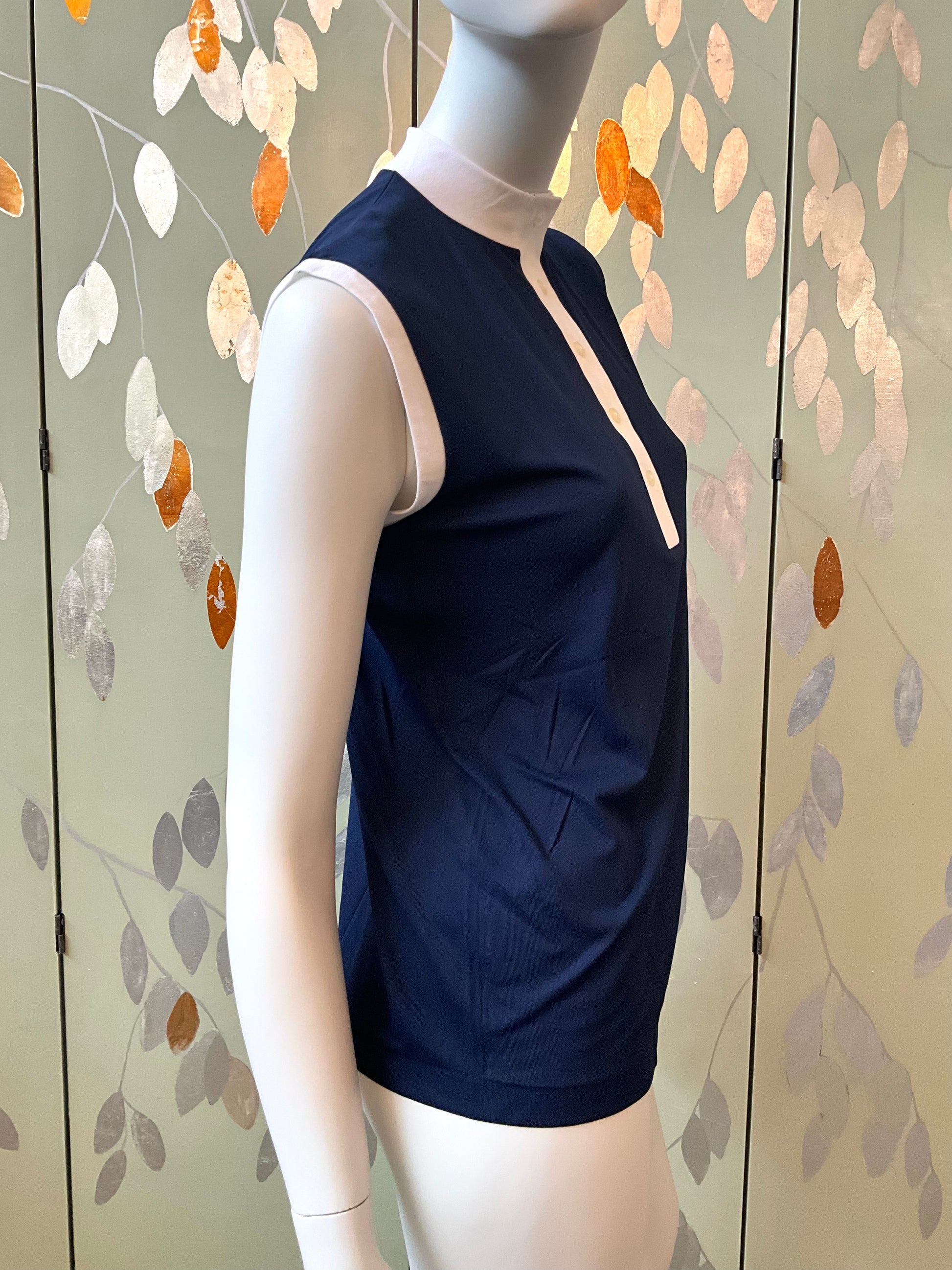 Navy sleeveless top on a mannequin against a decorative wall.