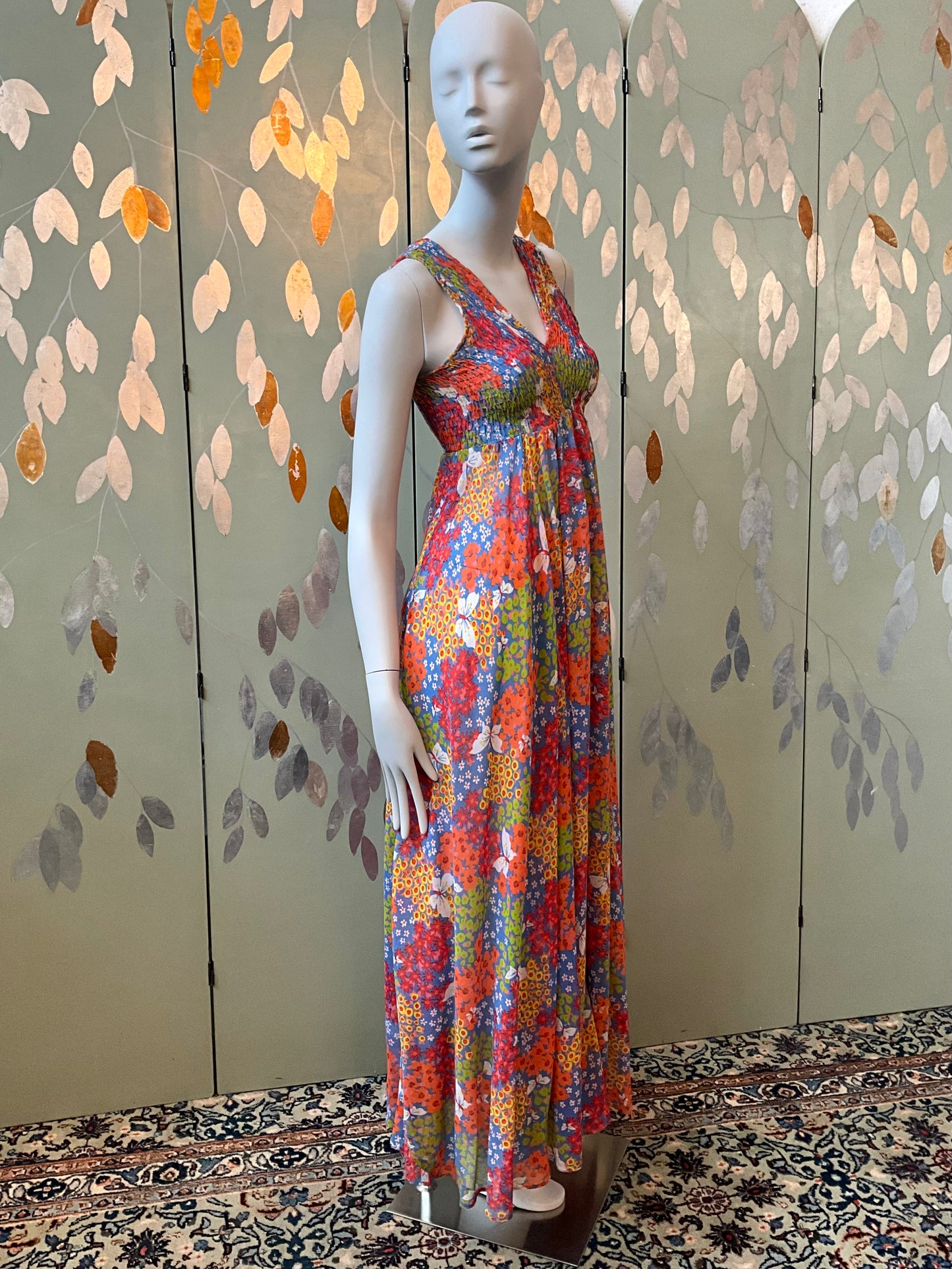 Mannequin wearing a colorful floral dress against a decorative wall.