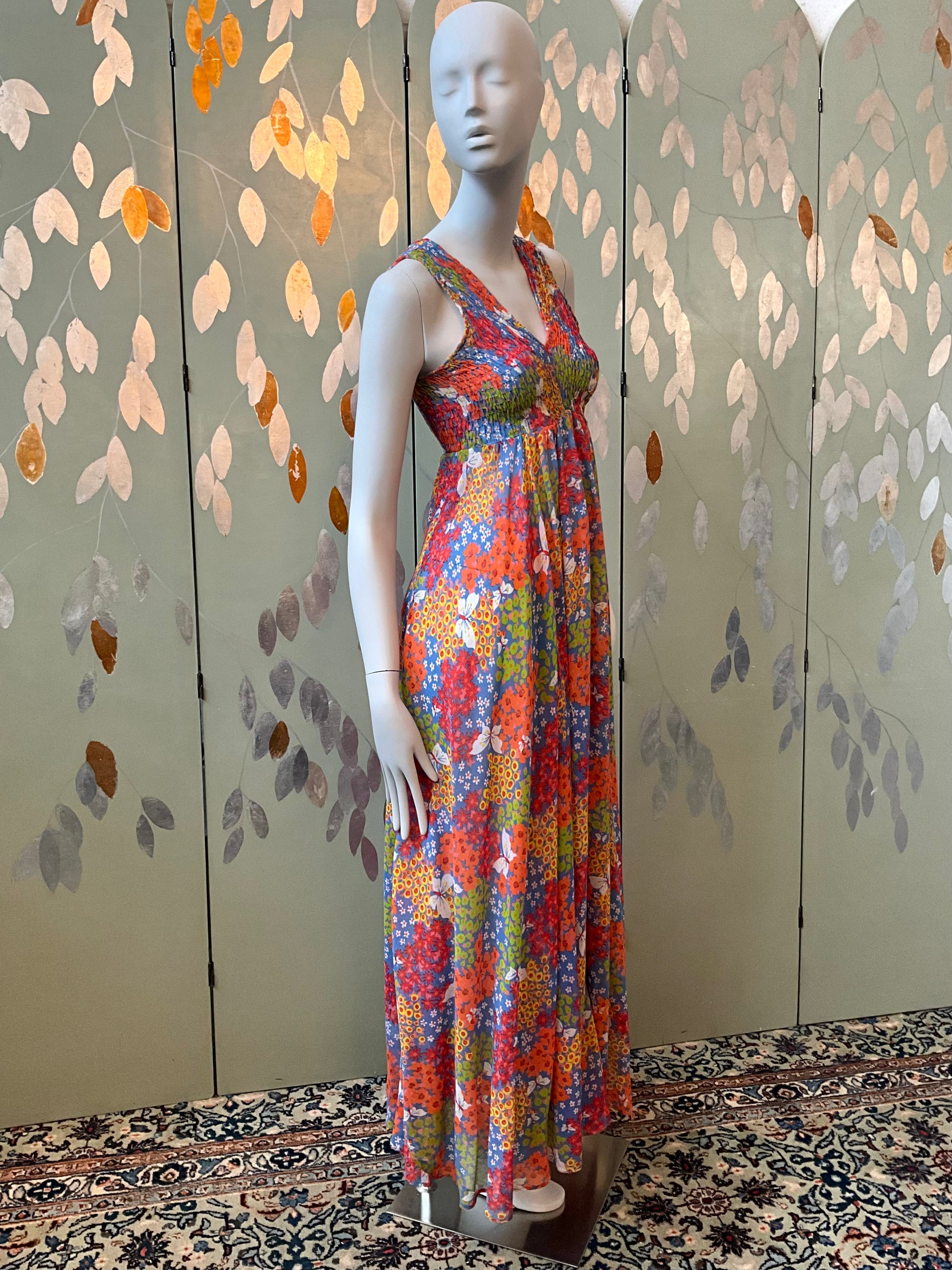 Mannequin wearing a colorful floral dress against a decorative wall.