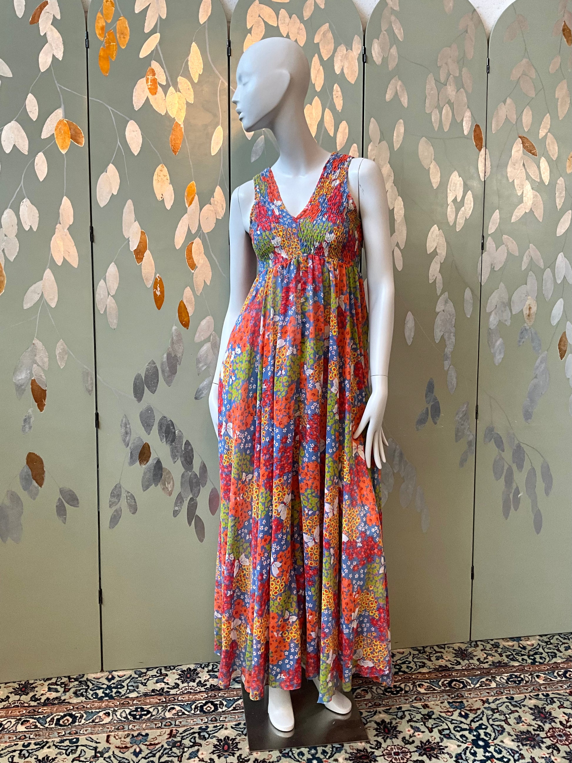 Mannequin wearing a colorful floral dress against a decorative wall.