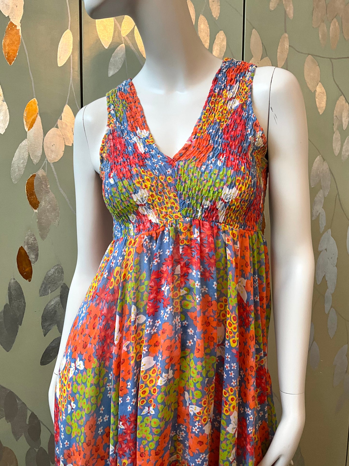 Colorful floral dress on a mannequin against a patterned wall.