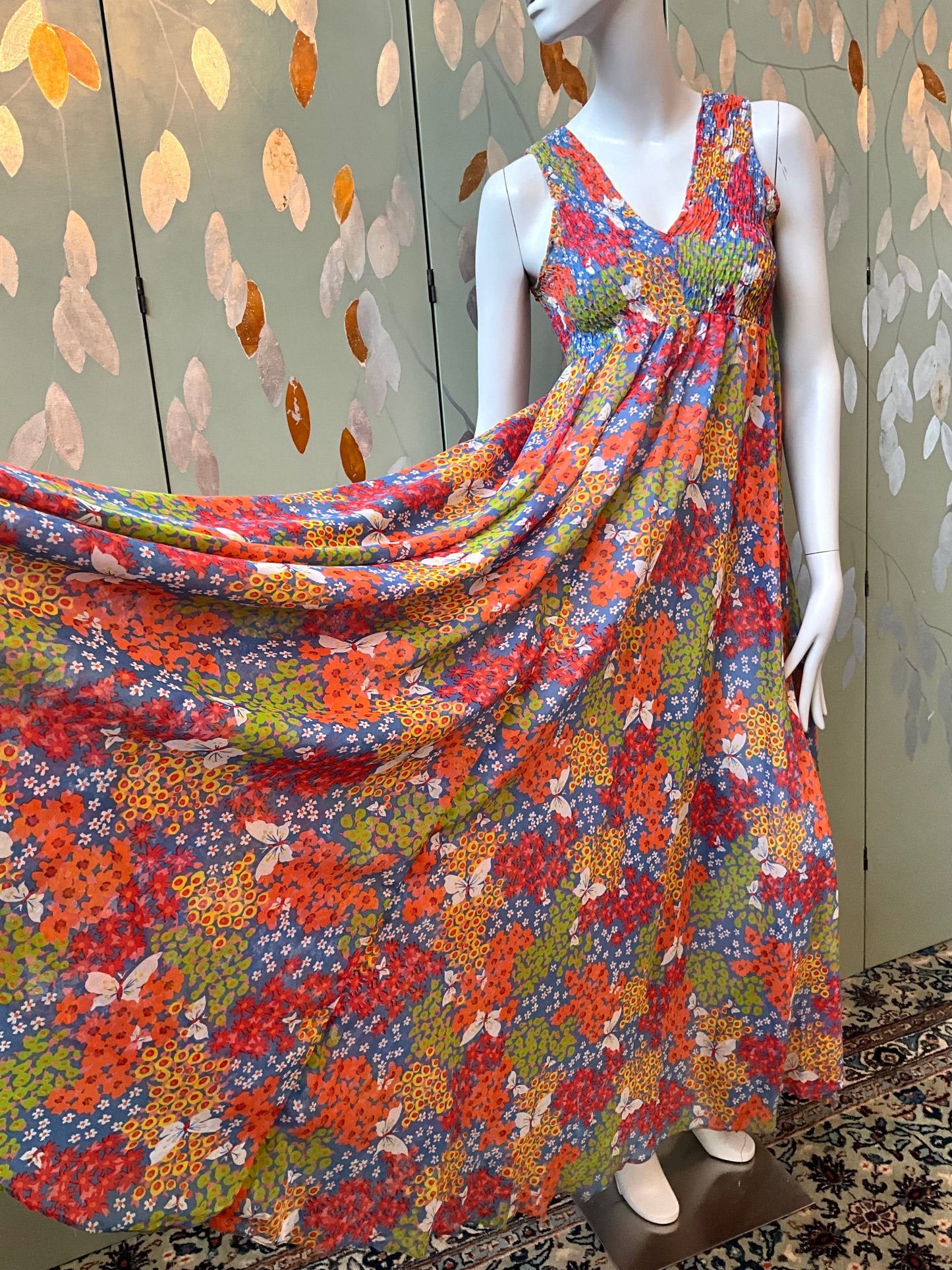 Mannequin wearing a colorful floral dress against a patterned wall.