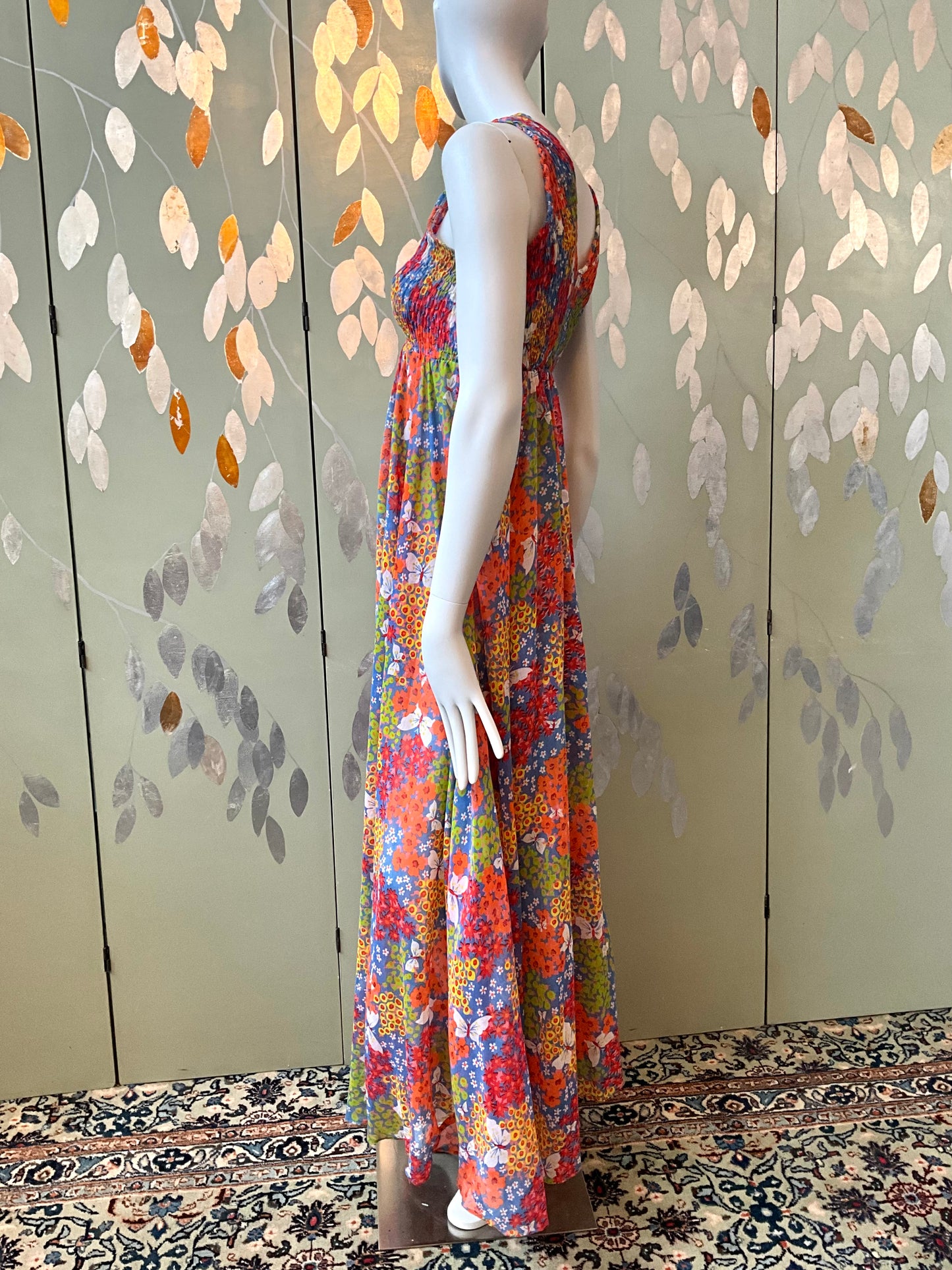 Mannequin wearing a colorful floral dress against a patterned wall.