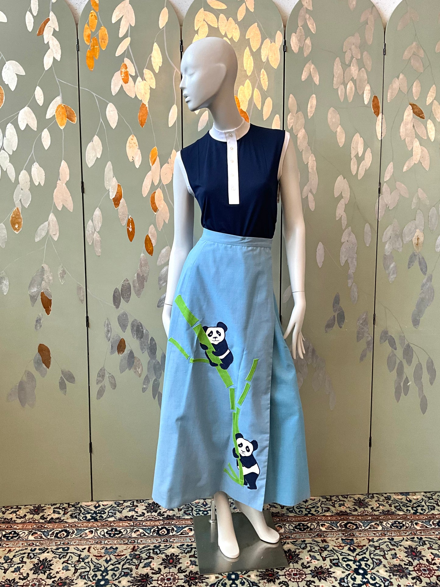 Mannequin wearing a navy top and light blue skirt with panda designs against a decorative wall.