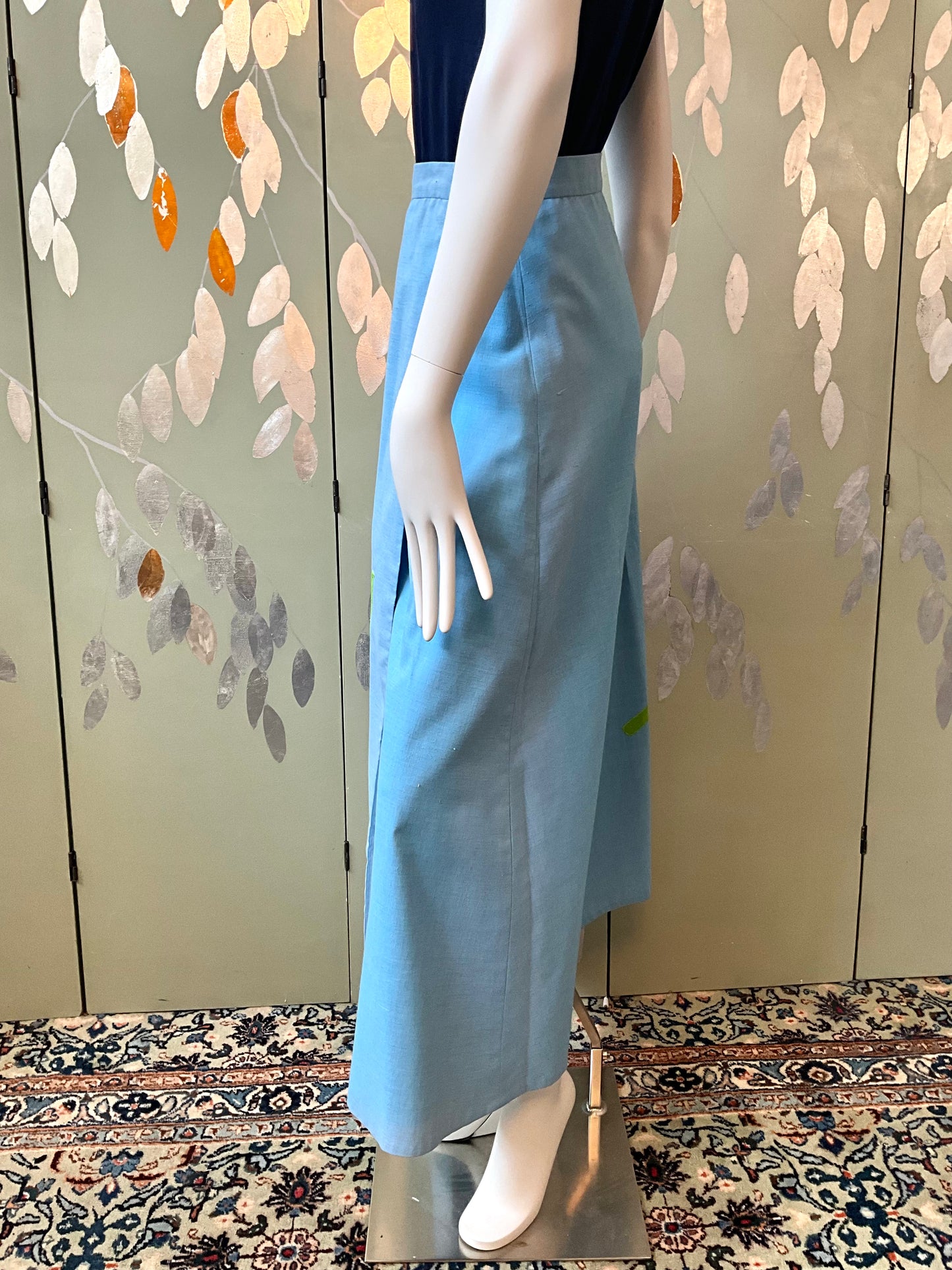 Mannequin wearing a light blue skirt against a decorative wall.