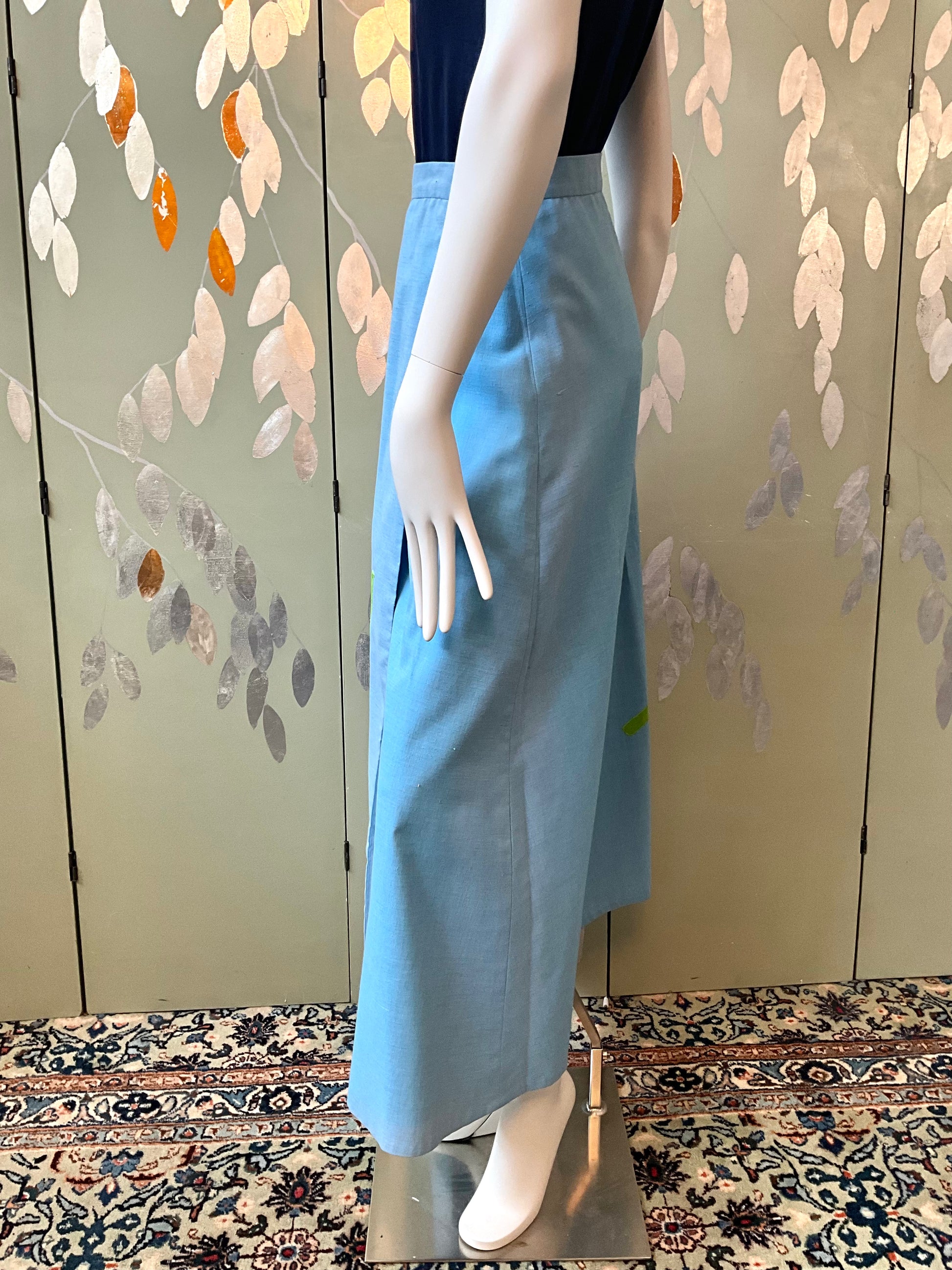 Mannequin wearing a light blue skirt against a decorative wall.