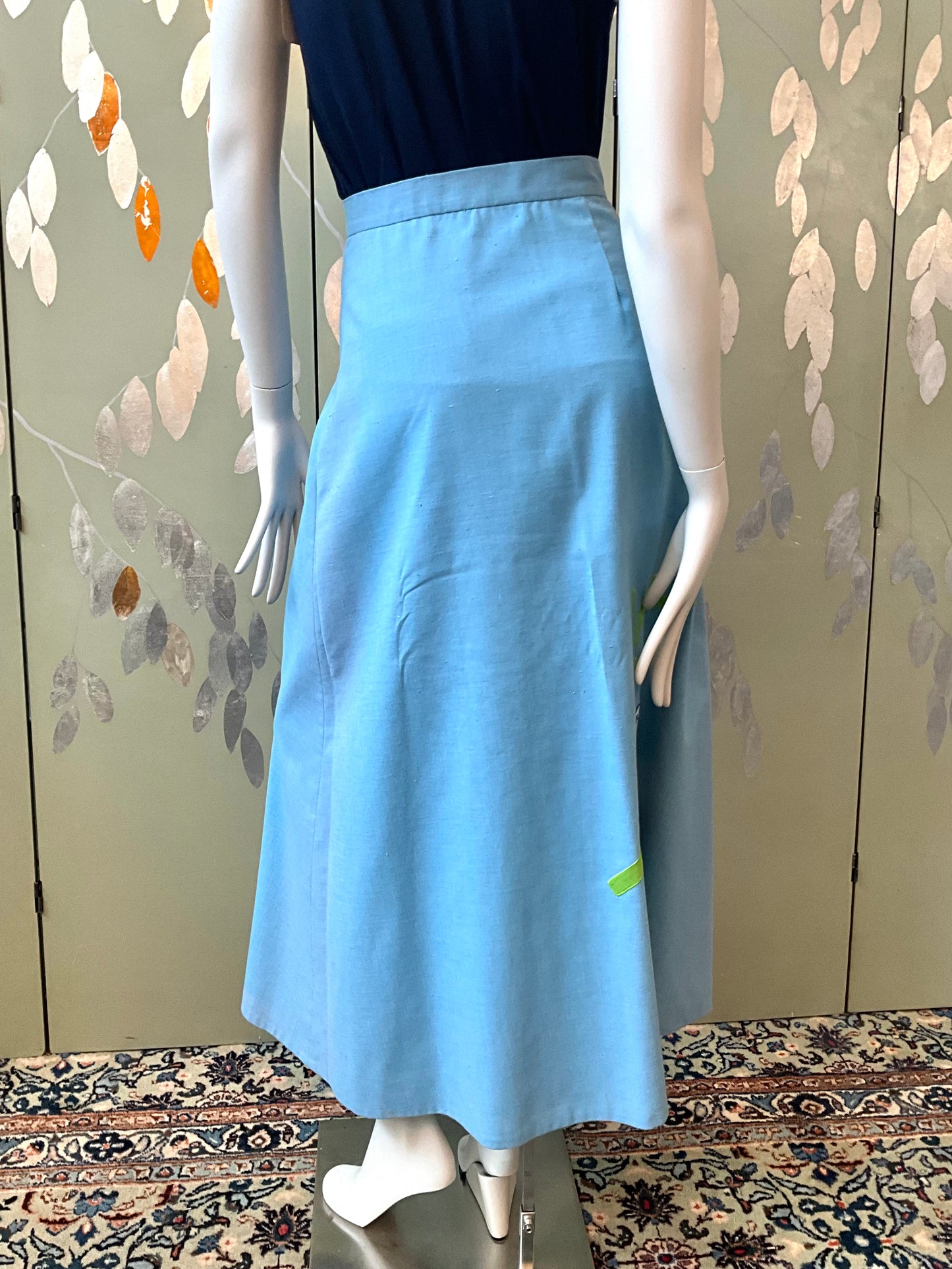 Mannequin wearing a blue skirt with a floral patterned wall in the background