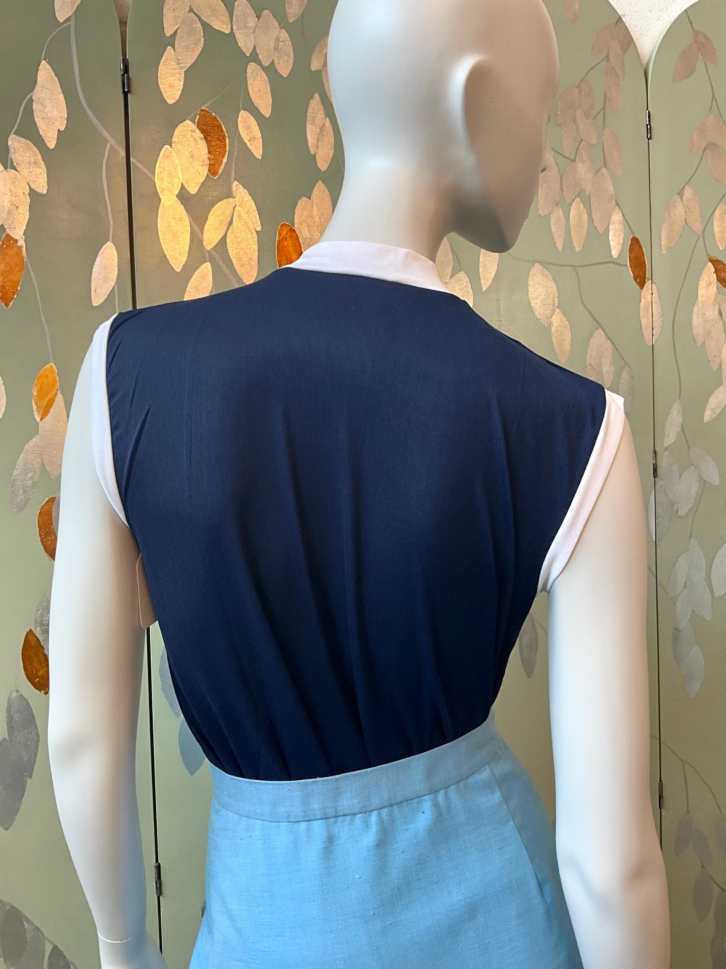 Mannequin wearing a navy top with a light blue skirt against a decorative wall.