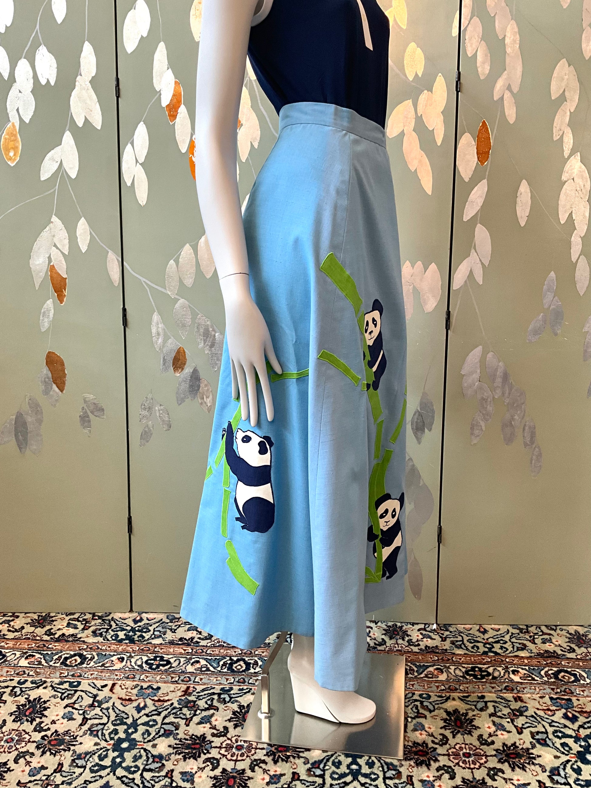 Mannequin wearing a light blue skirt with panda designs against a decorative wall.