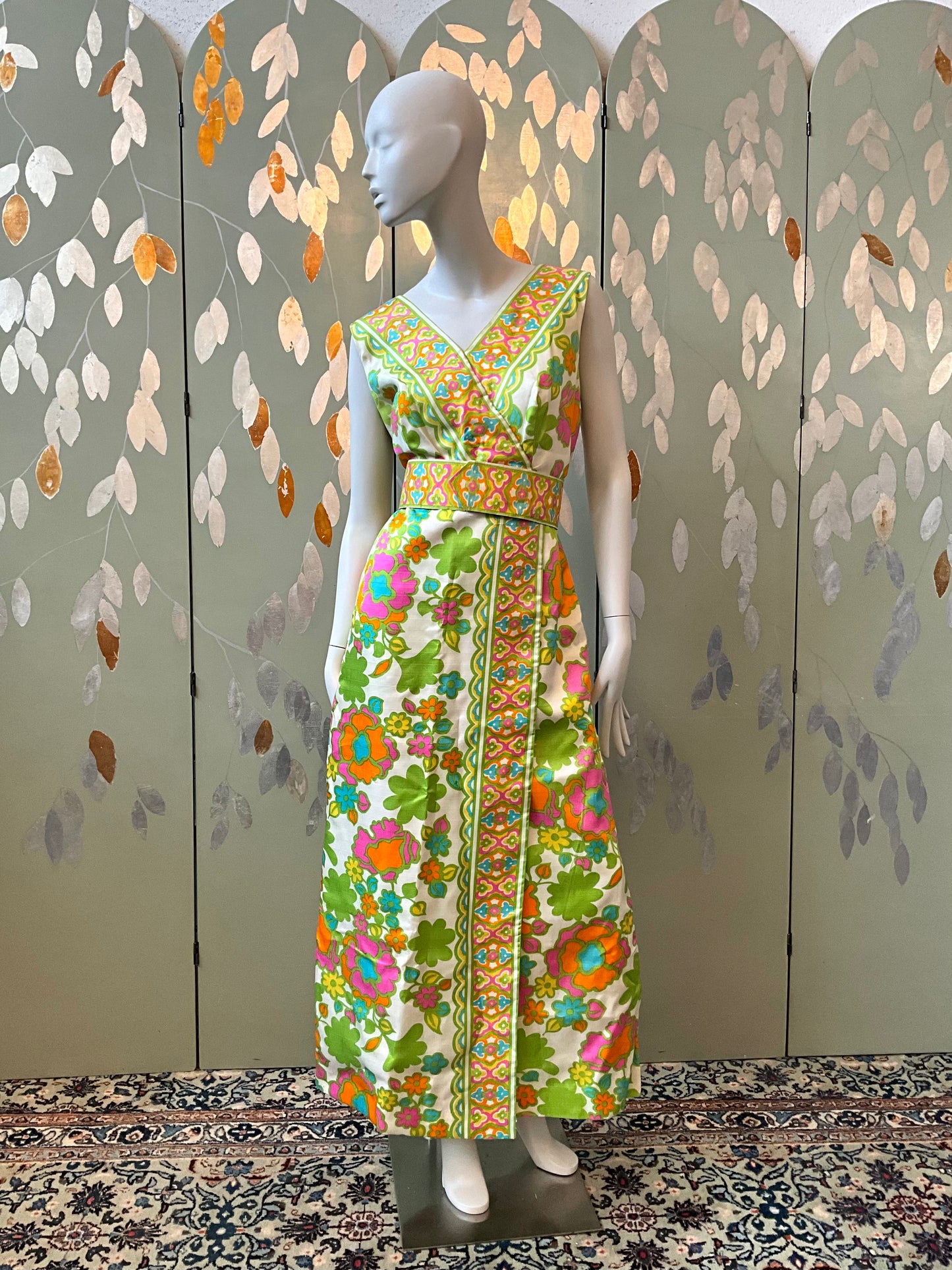 Mannequin wearing a floral dress against a decorative wall.