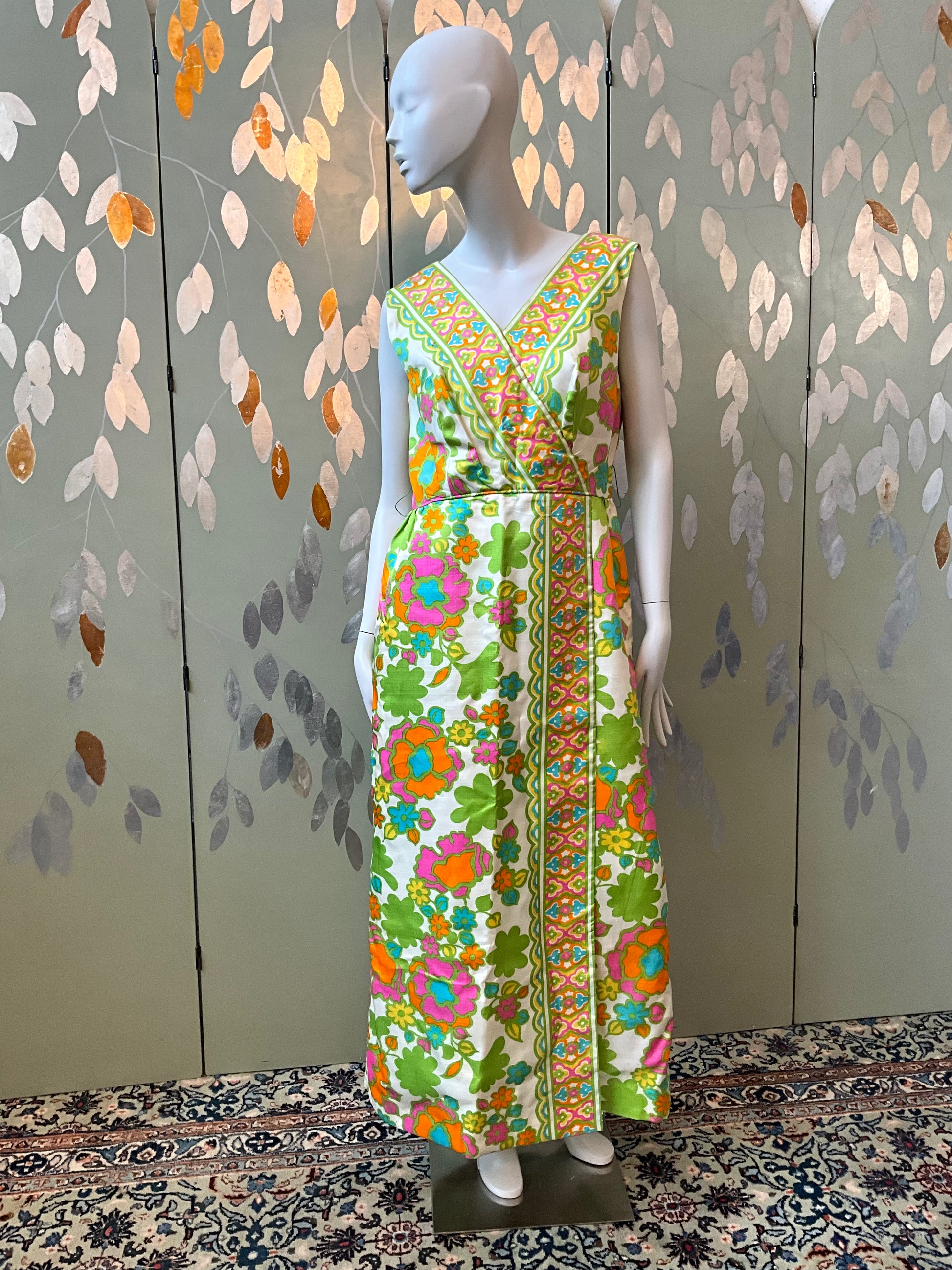 Mannequin wearing a colorful floral dress against a patterned wall.