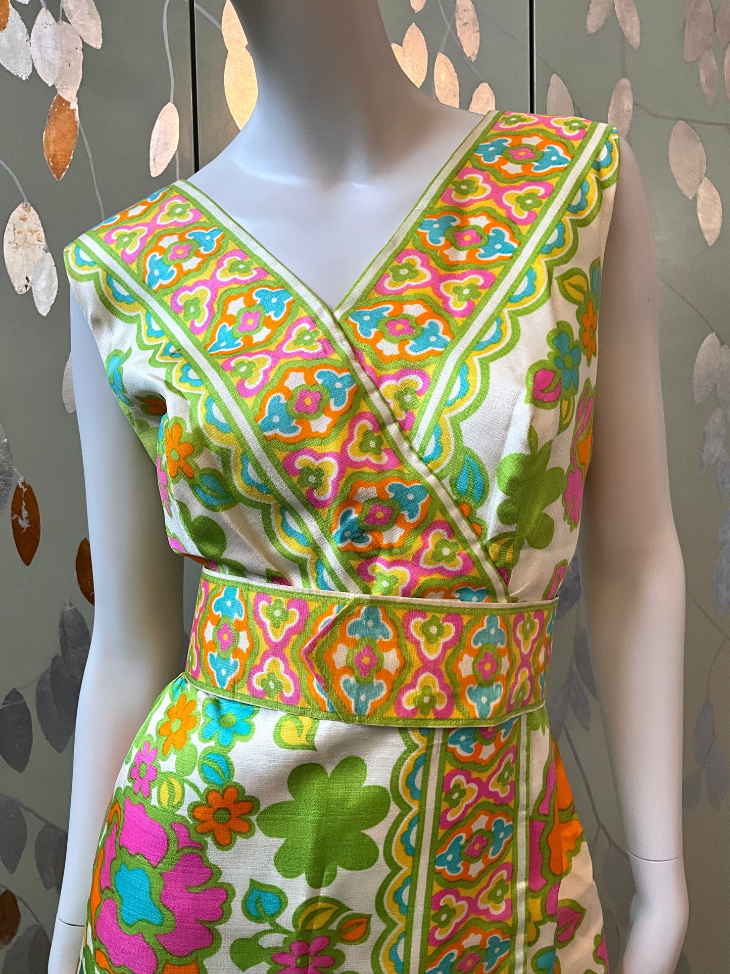 Colorful patterned dress on a mannequin against a decorative wall.