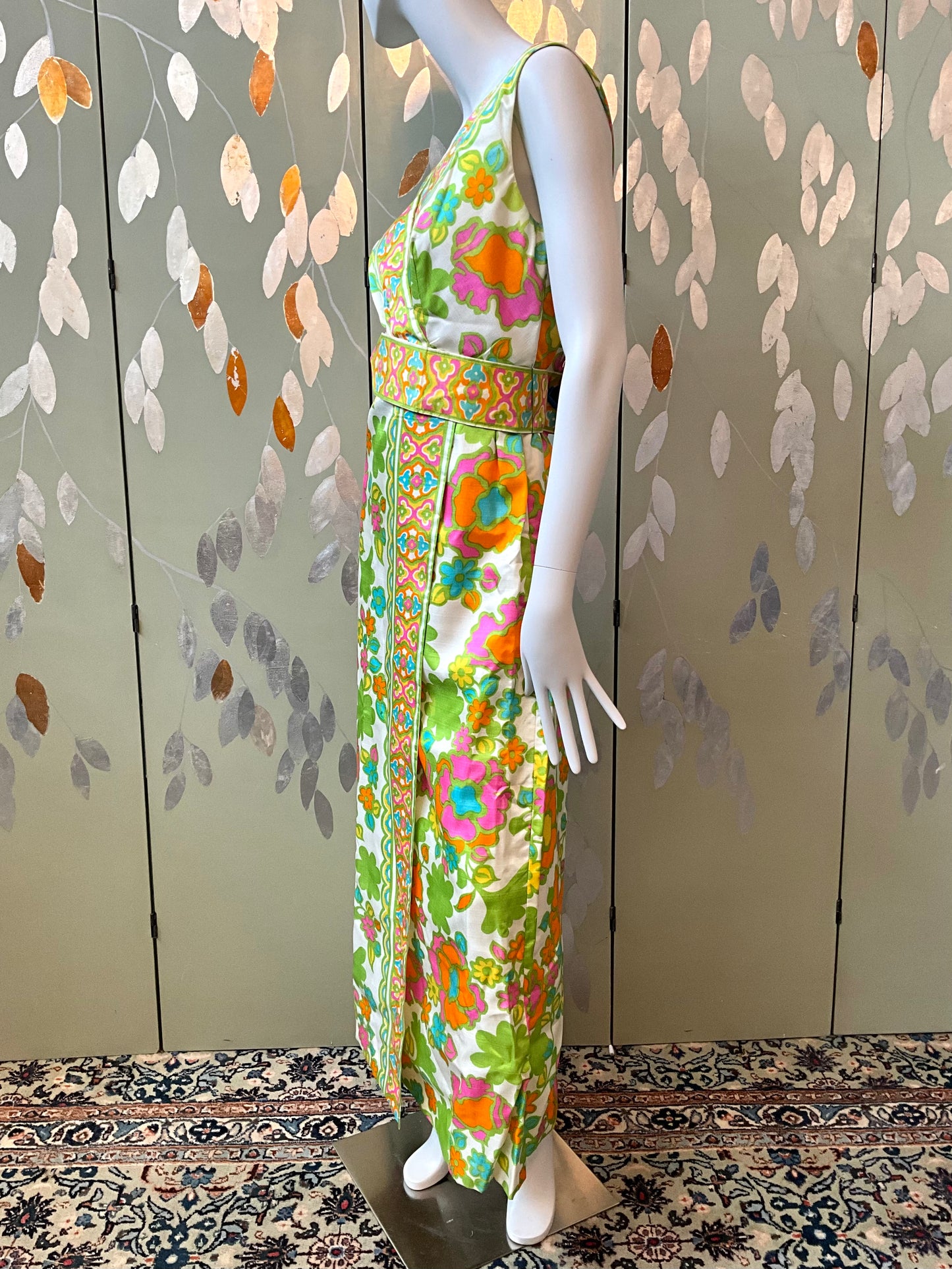 Mannequin wearing a colorful floral dress against a patterned wall.