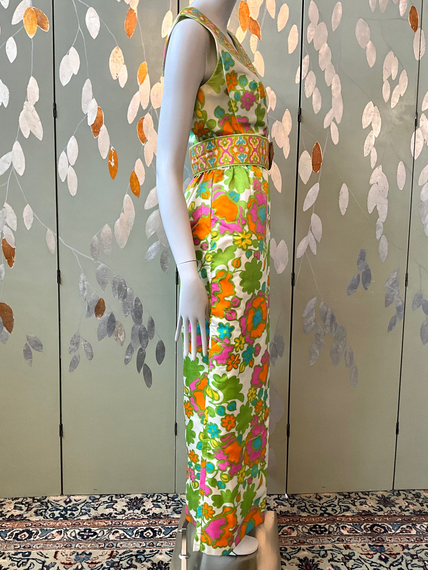 Mannequin wearing a colorful floral dress against a patterned wall.