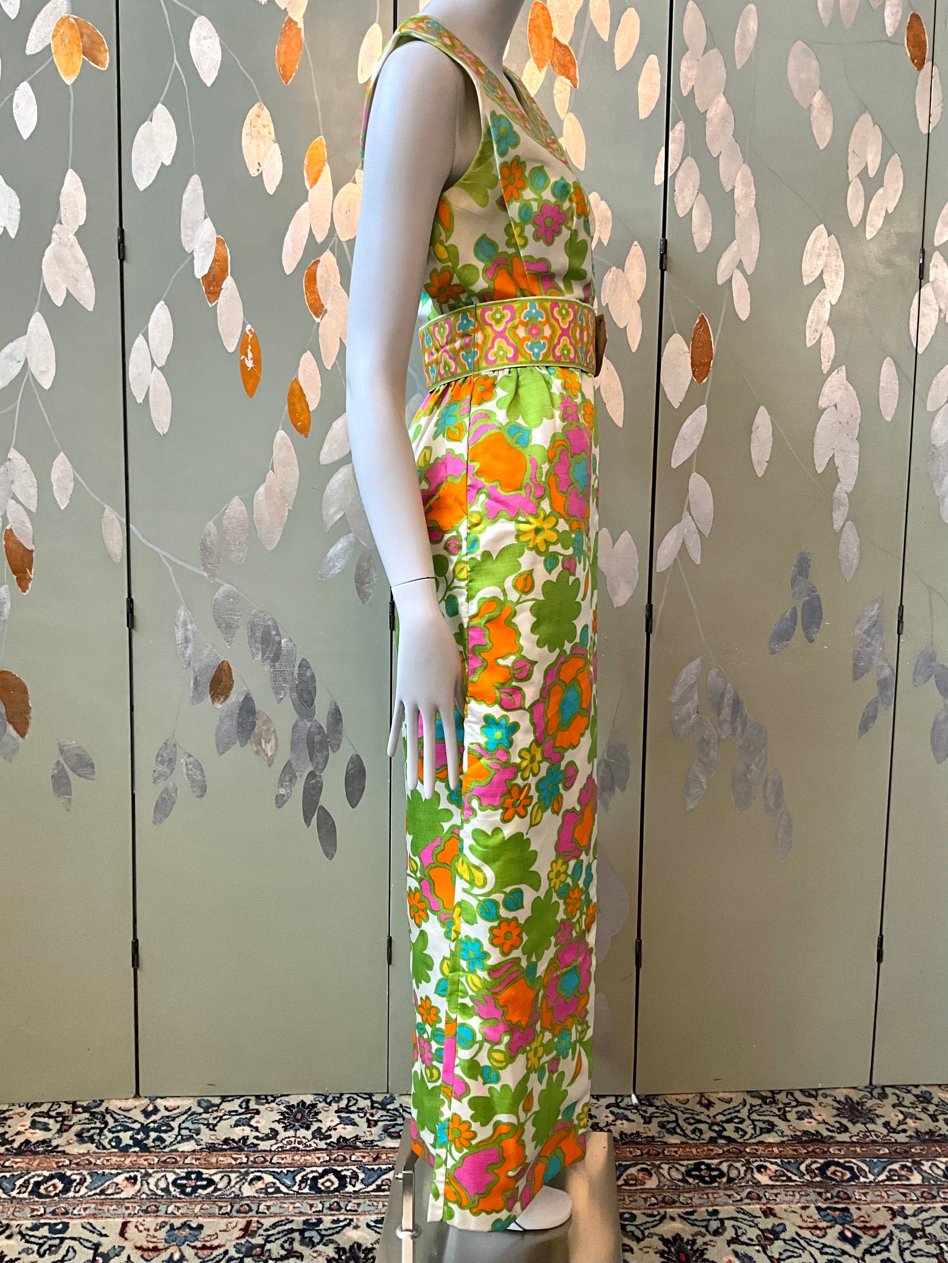 Mannequin wearing a colorful floral dress against a patterned wall.