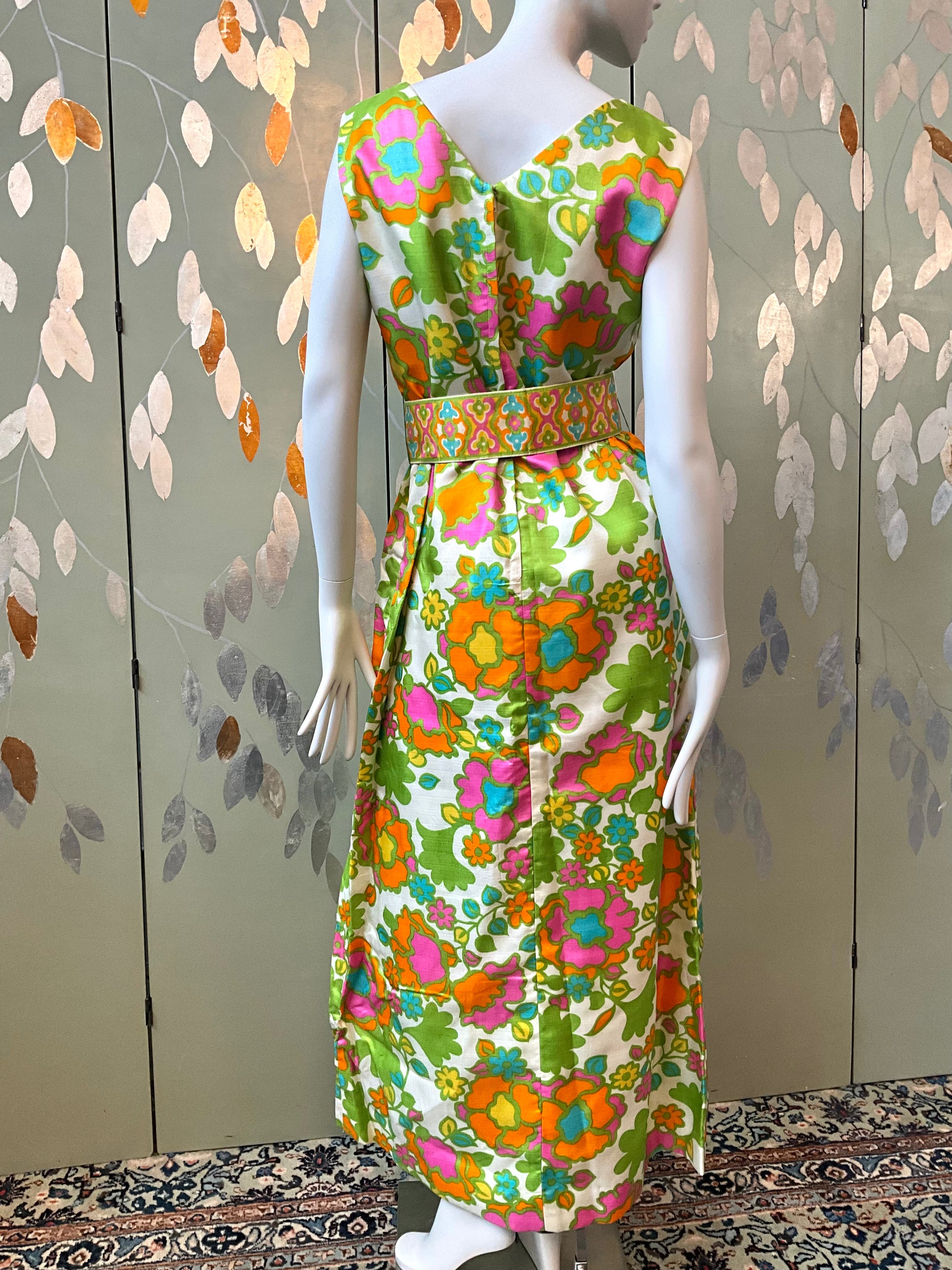 Mannequin wearing a colorful floral dress against a patterned wall.