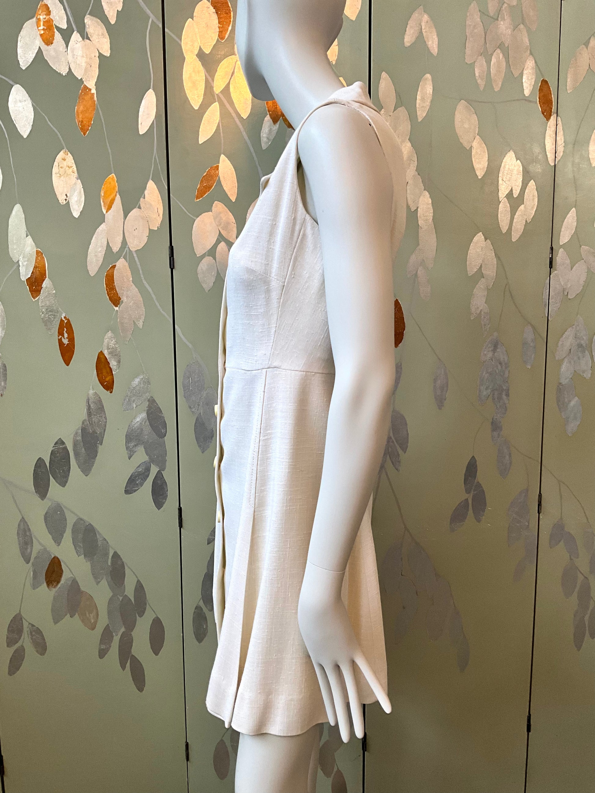 Mannequin wearing a white dress against a decorative wall with leaf patterns.