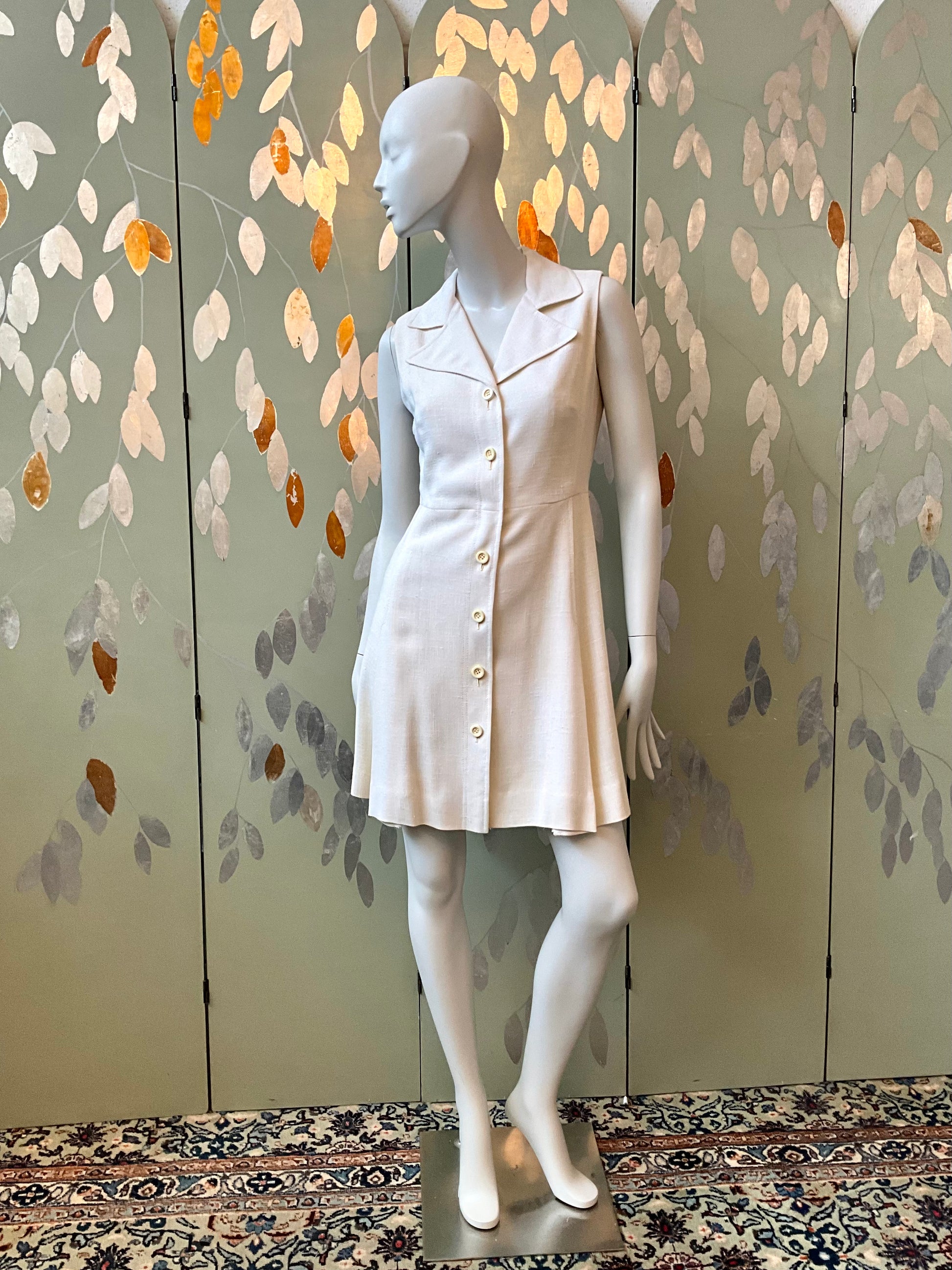 Mannequin wearing a white dress against a decorative wall with floral patterns.