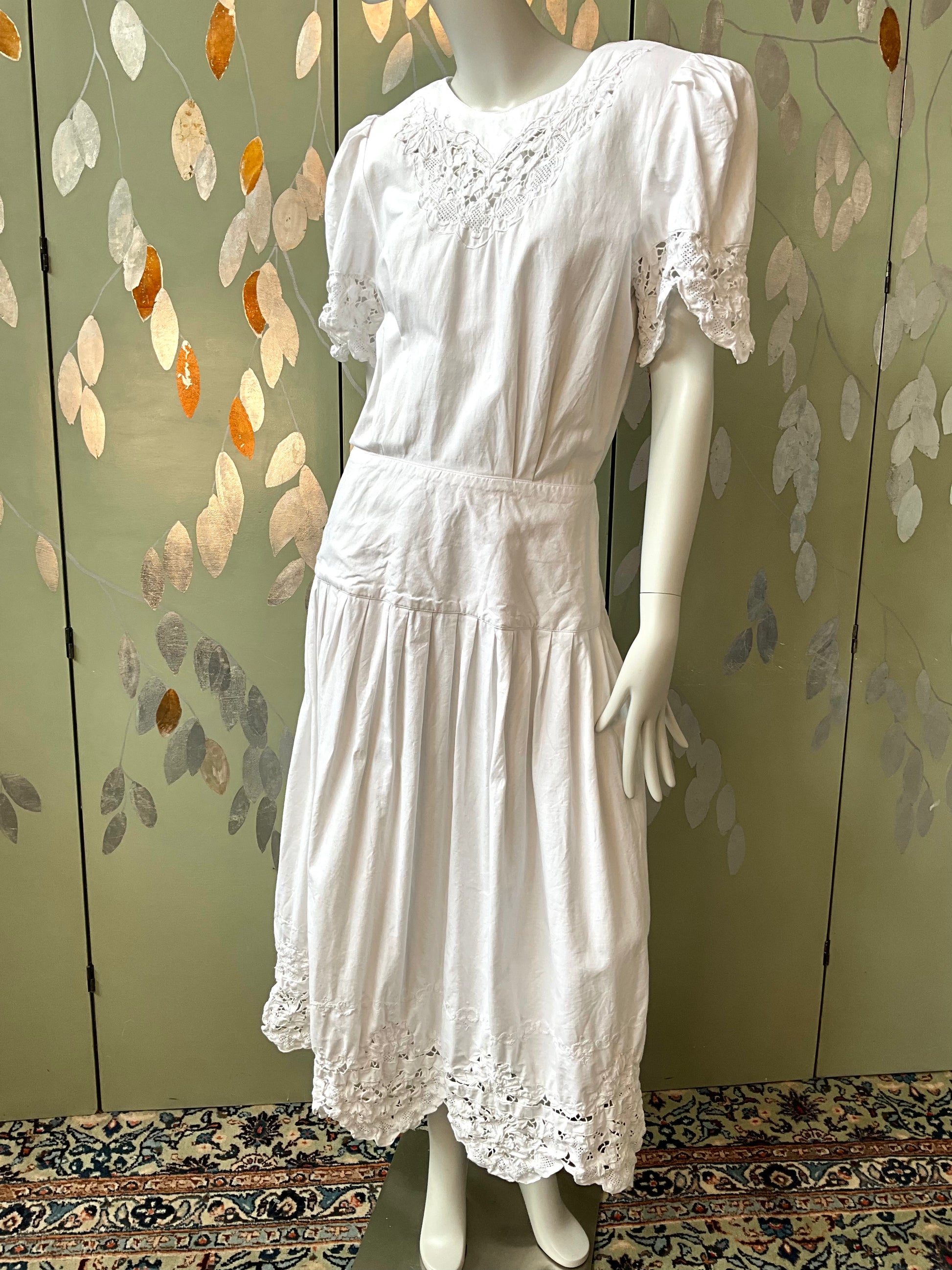 White lace dress on a mannequin against a decorative wall.