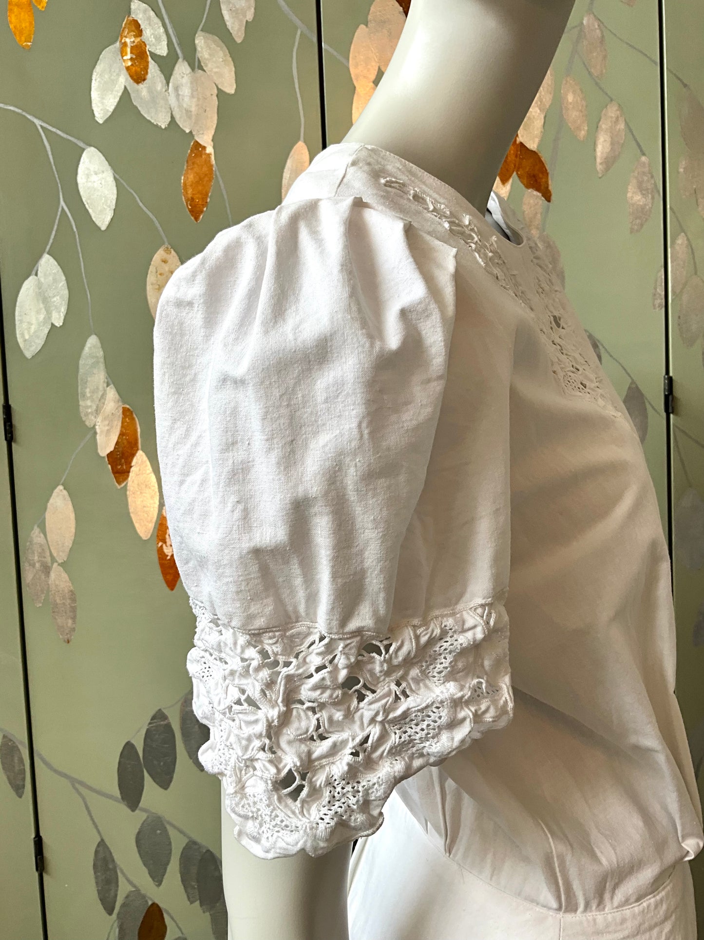 White lace dress on a mannequin against a decorative wall.