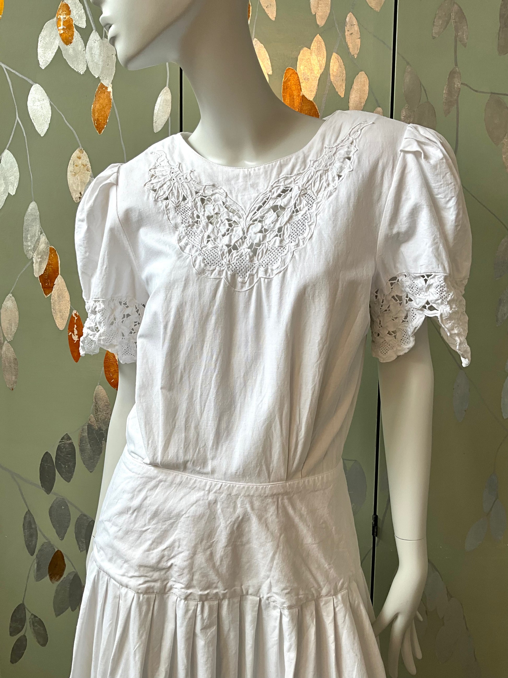 White lace dress on a mannequin against a decorative wall.