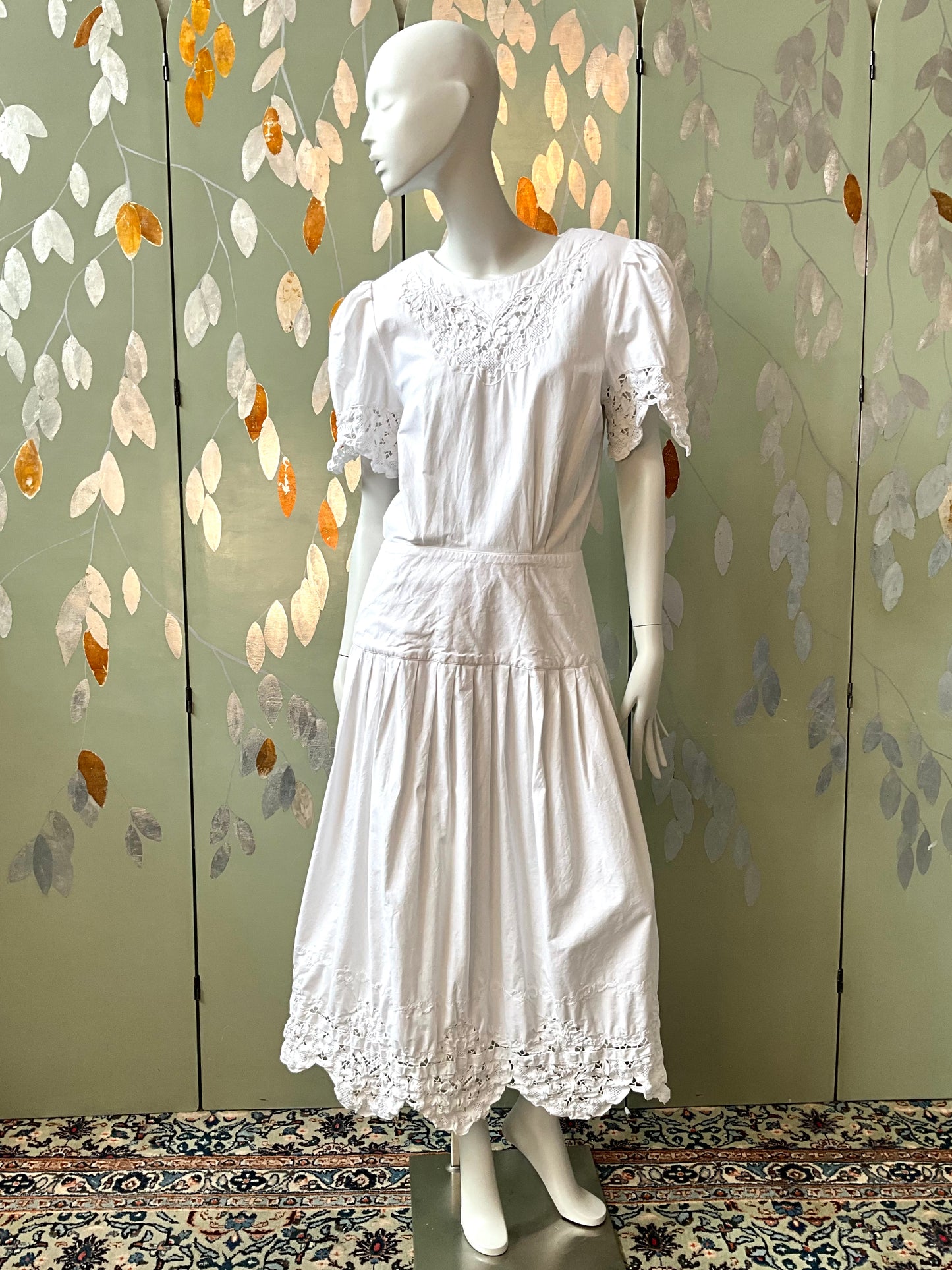 White dress on a mannequin against a decorative wall with leaf patterns.