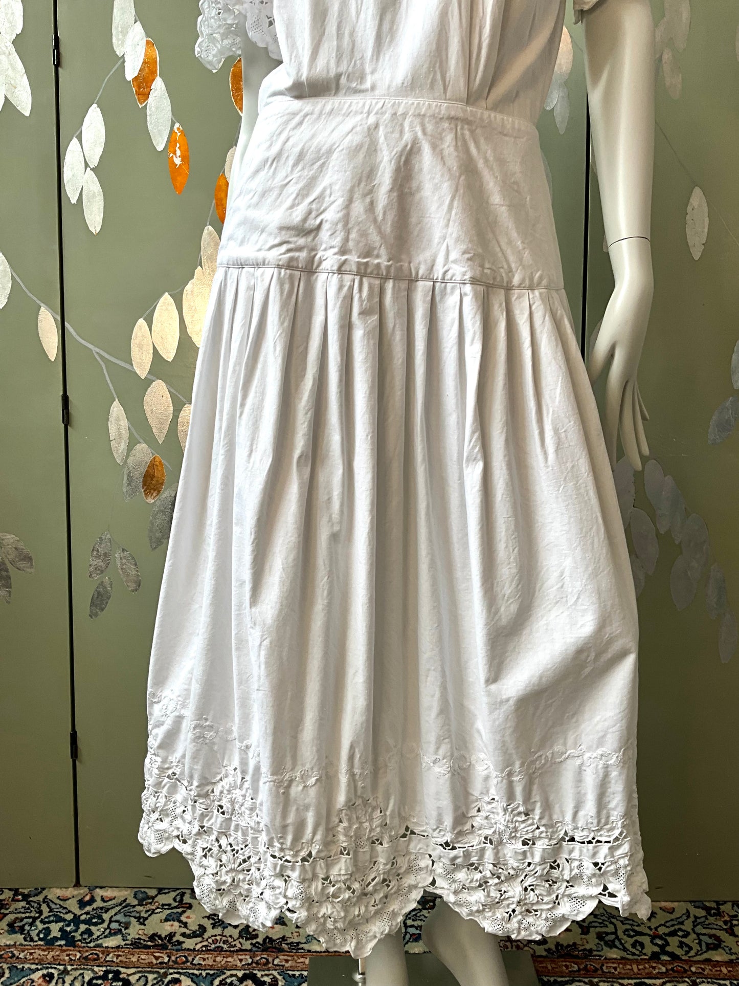 White dress on a mannequin against a decorative wall.