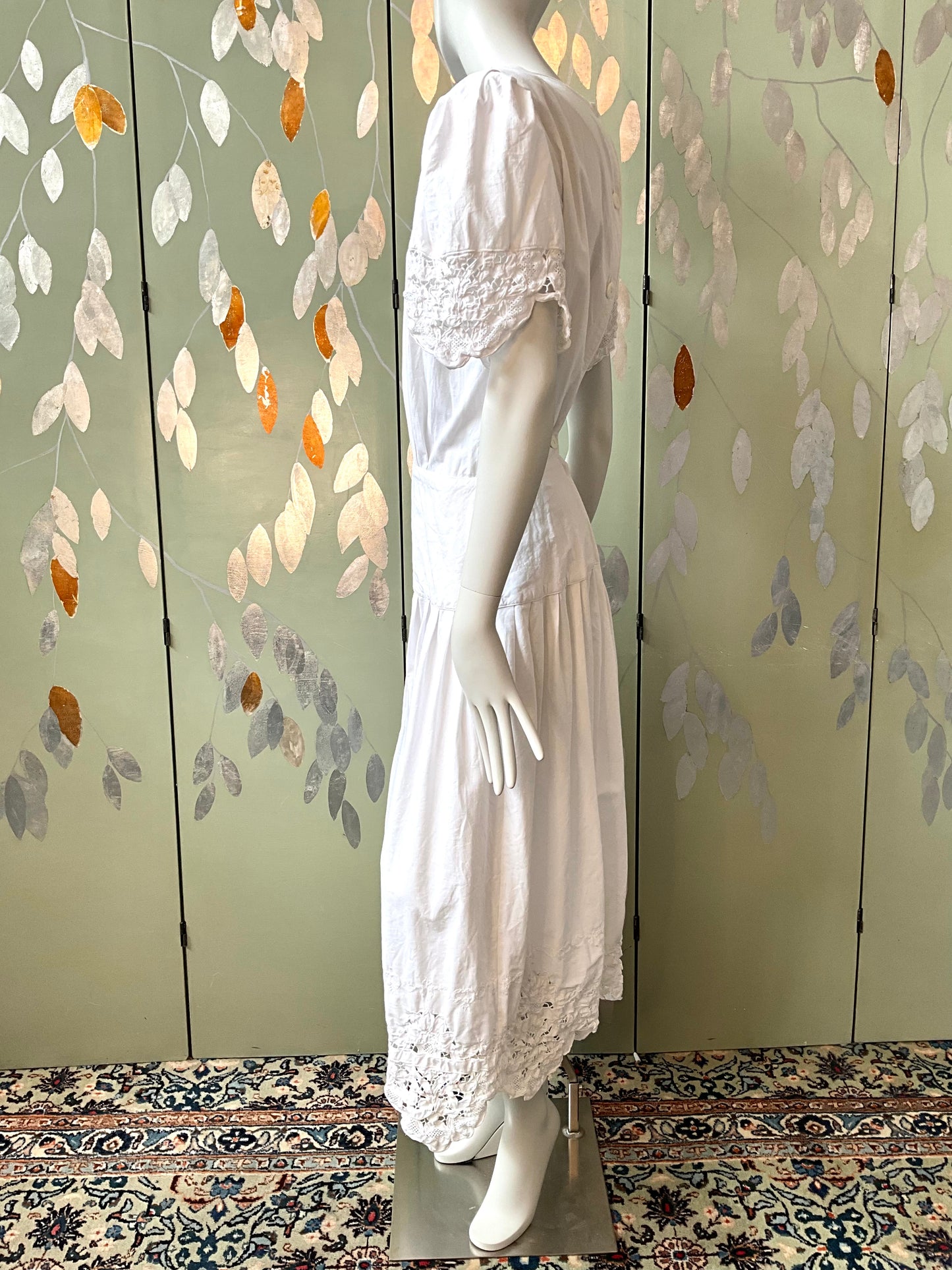 Mannequin wearing a white dress against a decorative wall with floral patterns.