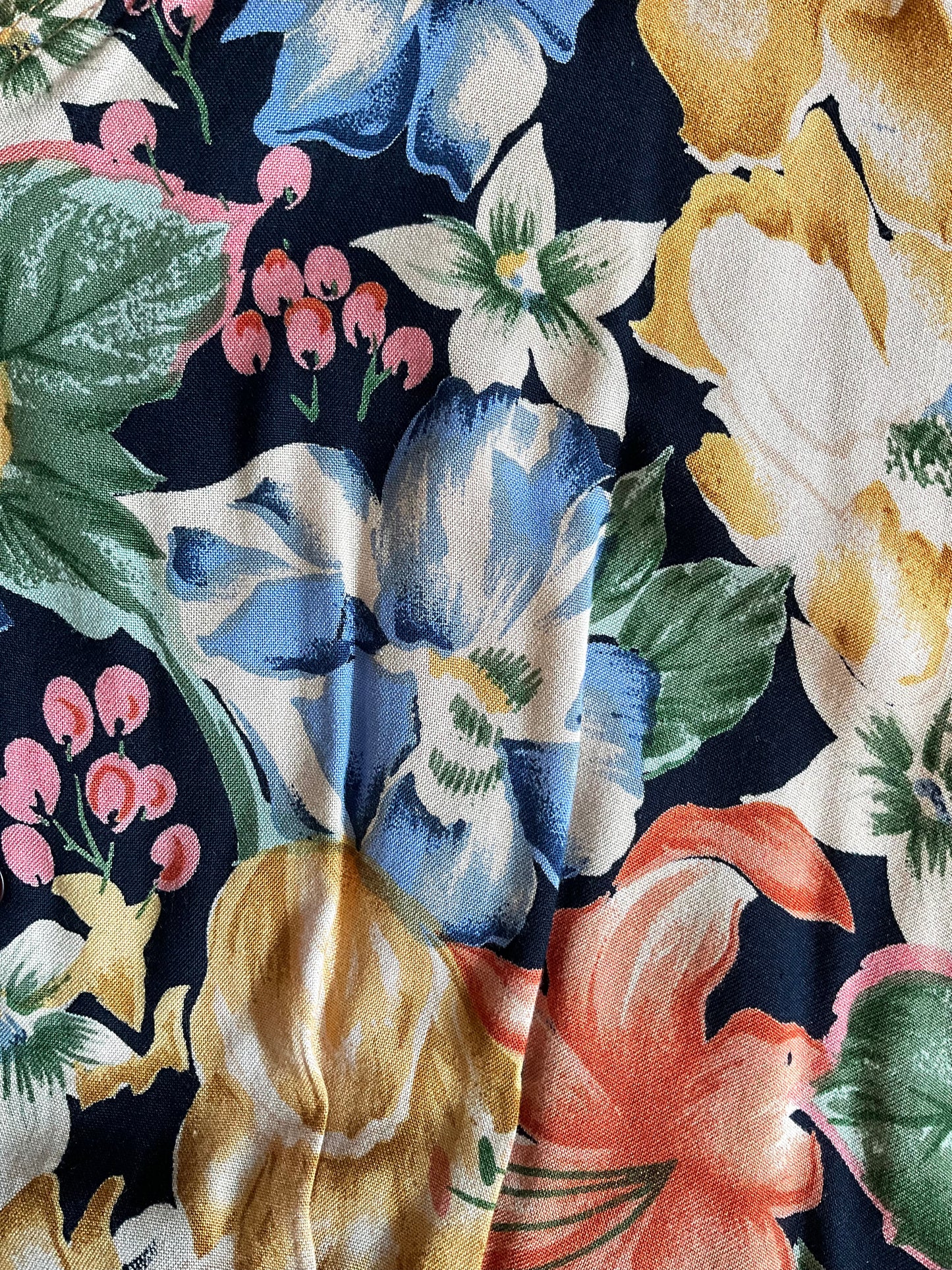 Close-up of a floral fabric pattern with blue, yellow, and pink flowers on a dark background.