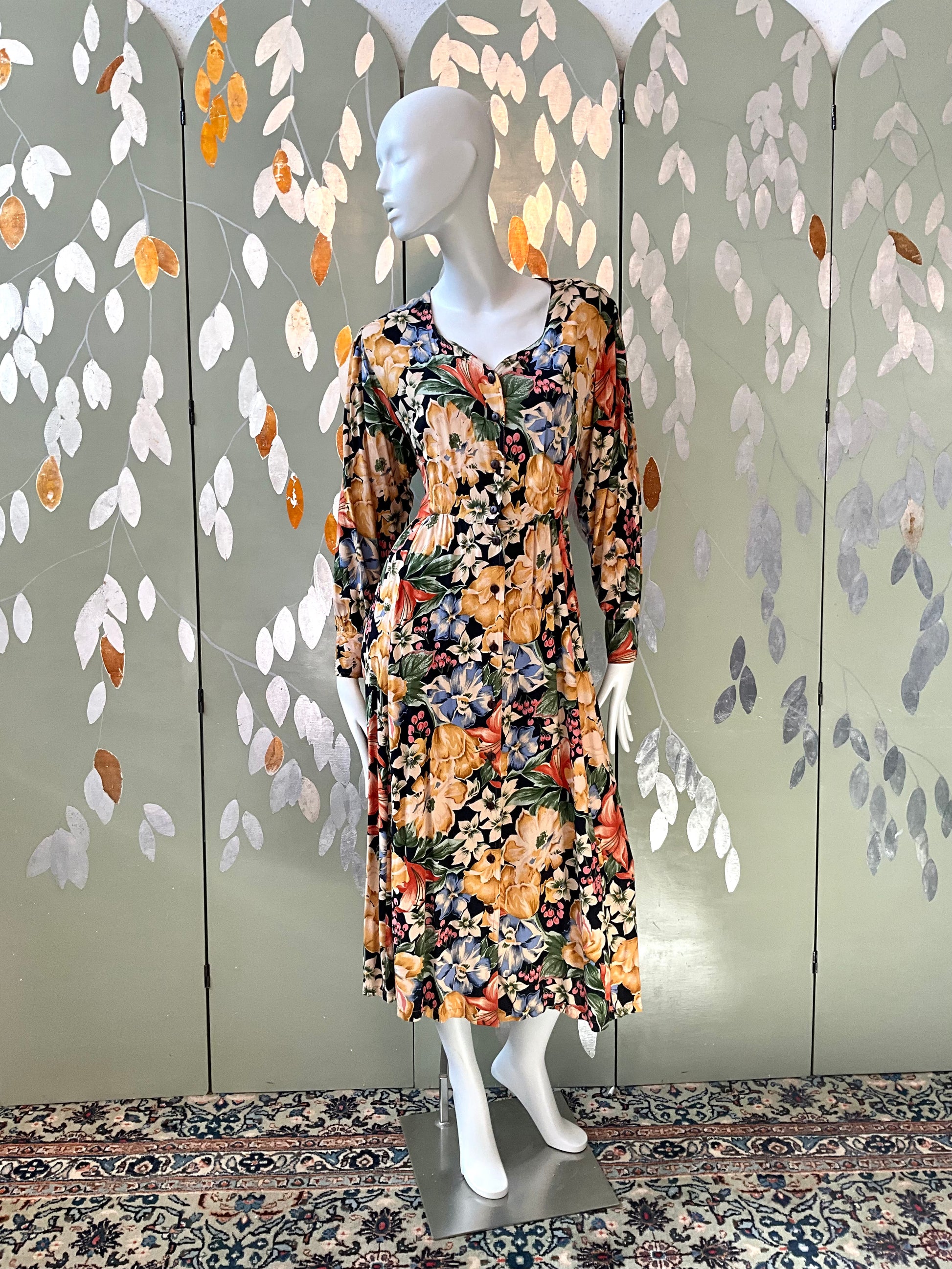 Mannequin wearing a floral dress against a decorative wall with leaf patterns.