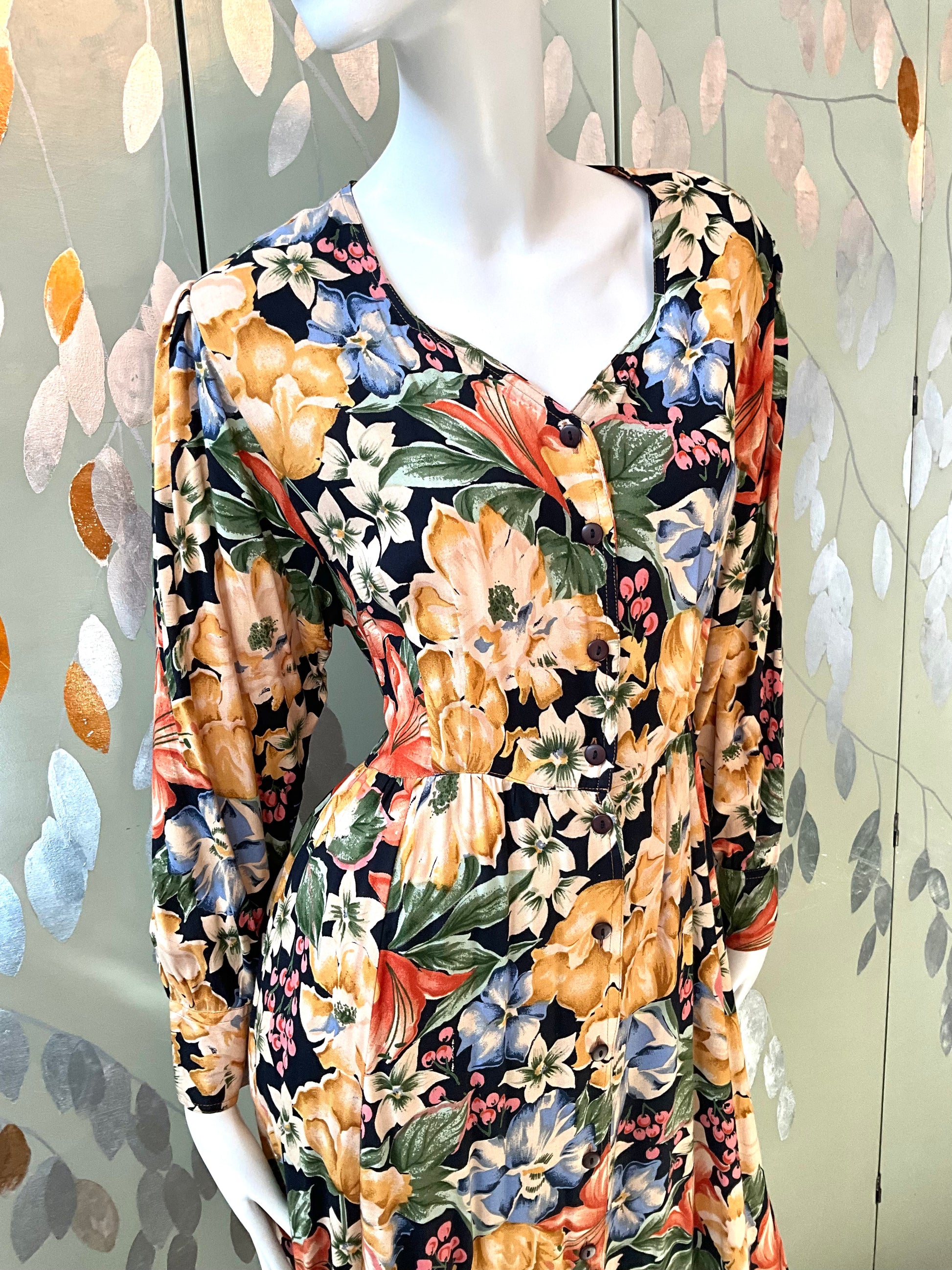 Mannequin wearing a floral dress with a colorful pattern against a decorative wall.