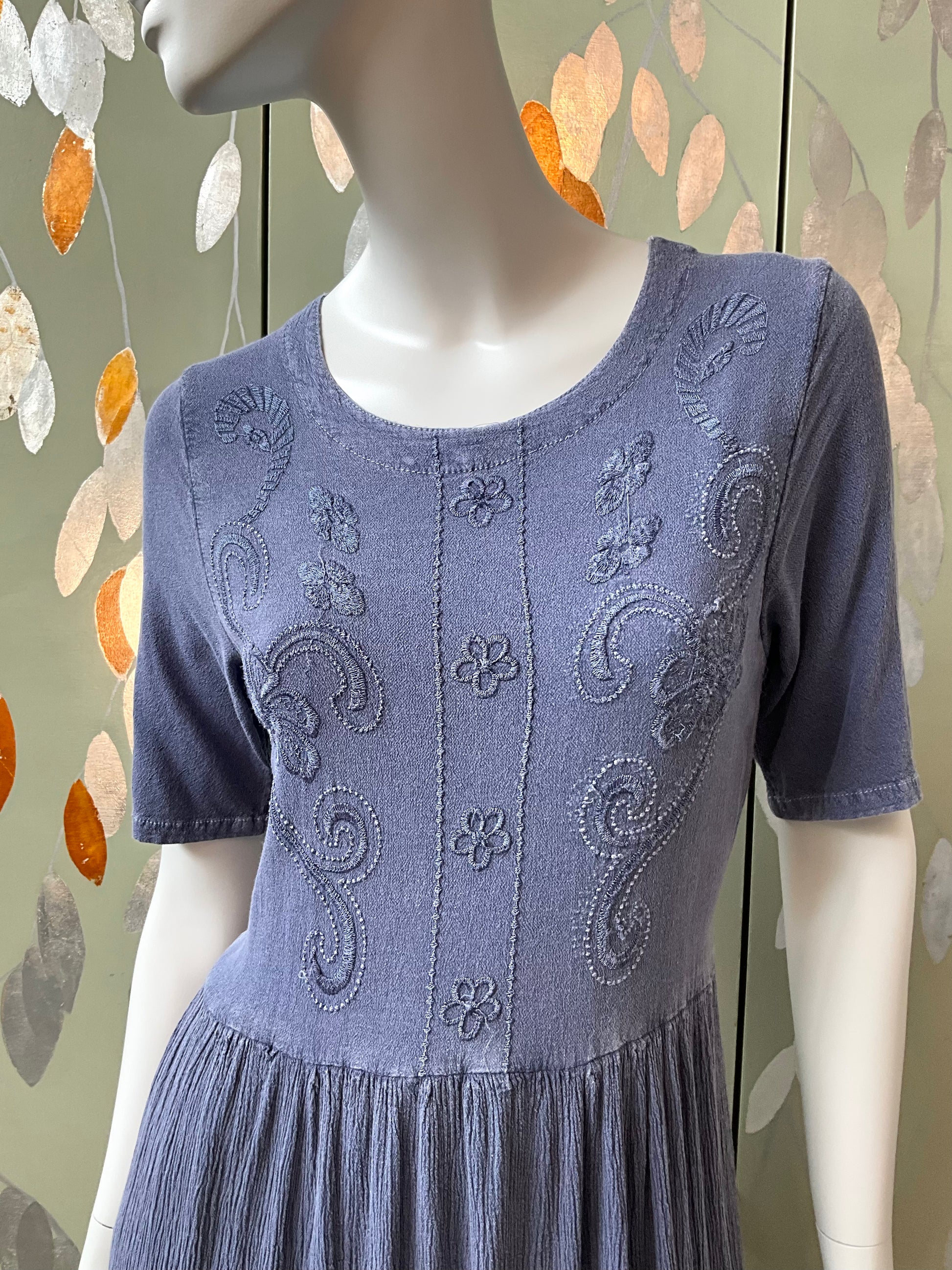 Blue dress with intricate embroidery on a mannequin against a decorative background