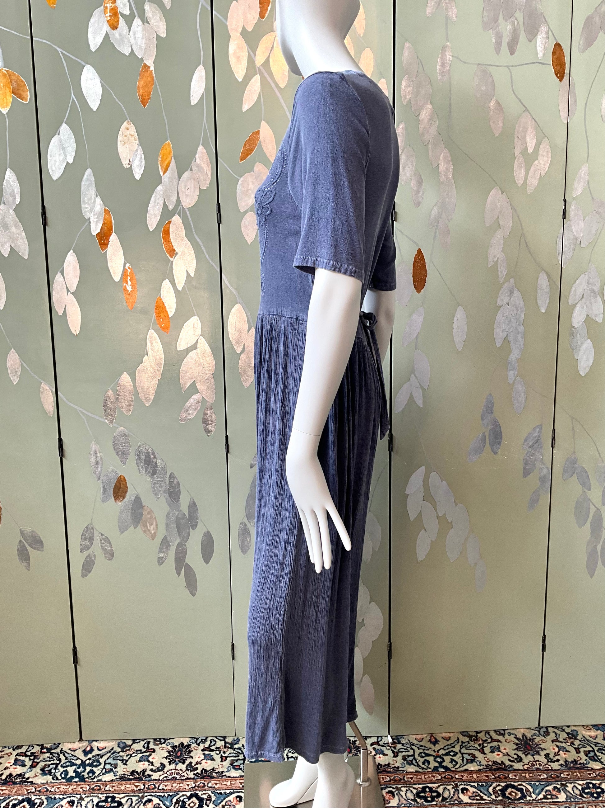 Mannequin wearing a blue dress against a decorative wall with leaf patterns.