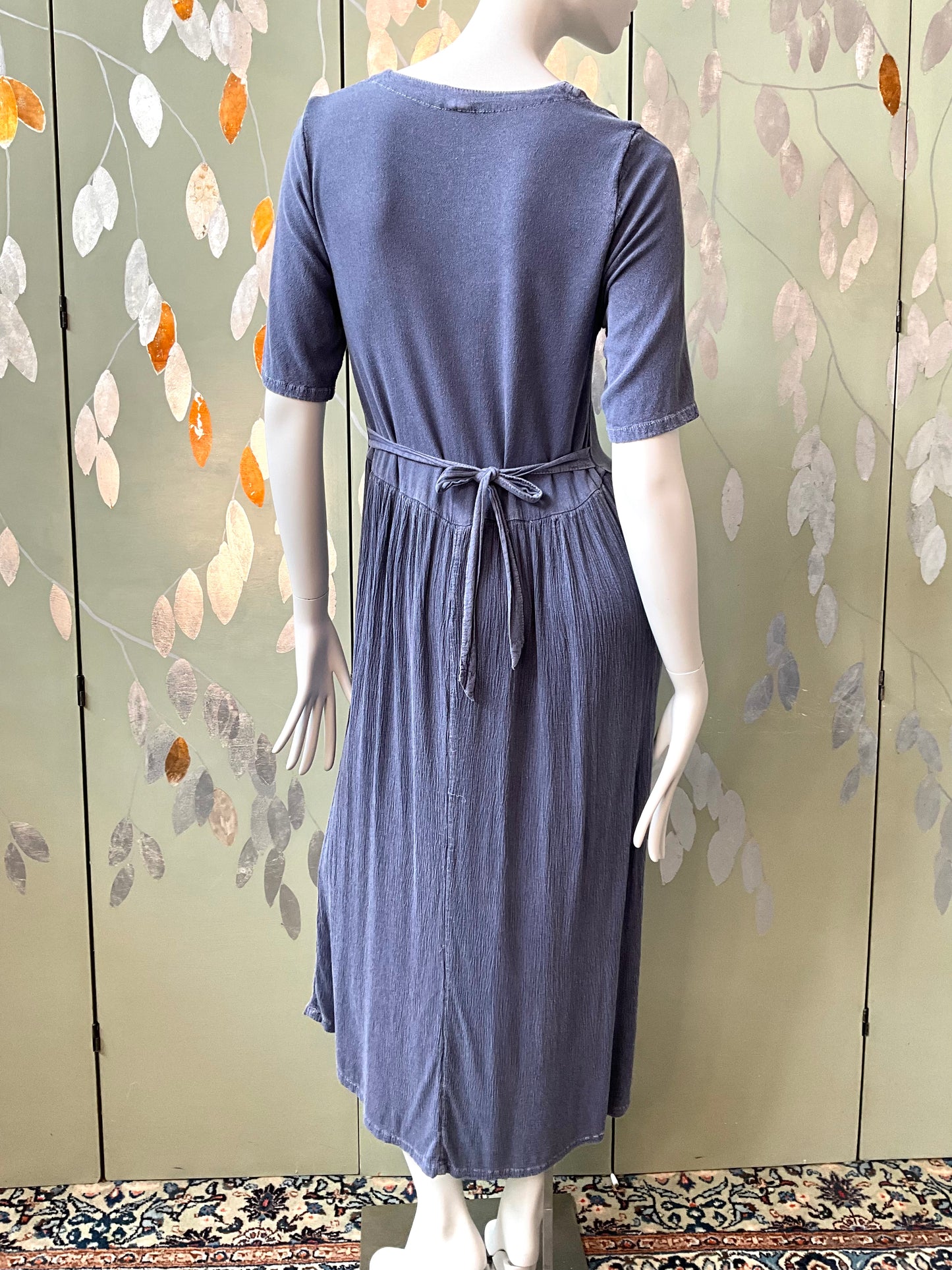 Mannequin wearing a blue dress against a floral-patterned wall.
