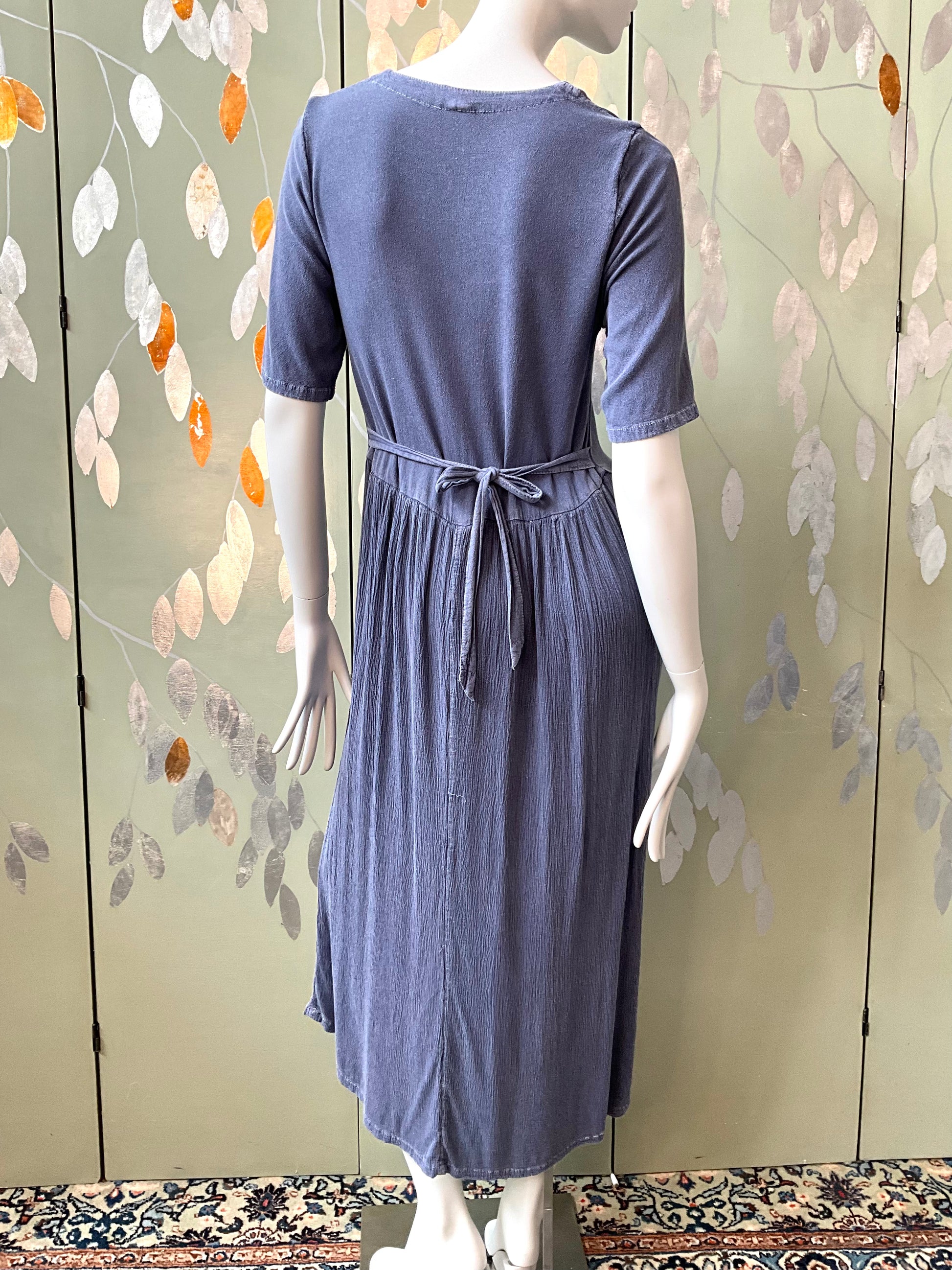 Mannequin wearing a blue dress against a floral-patterned wall.