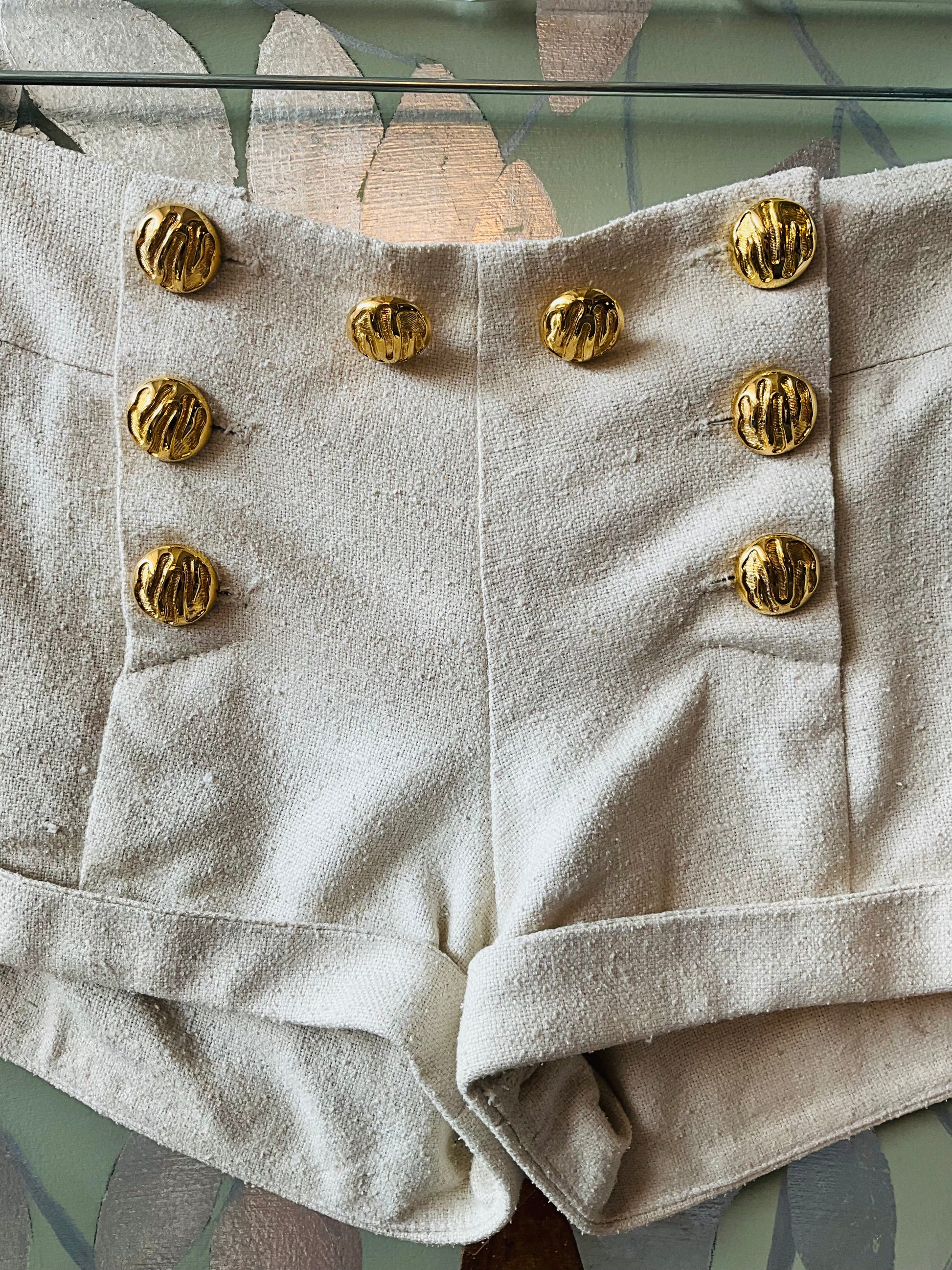 Beige shorts with gold buttons hanging on a wall 