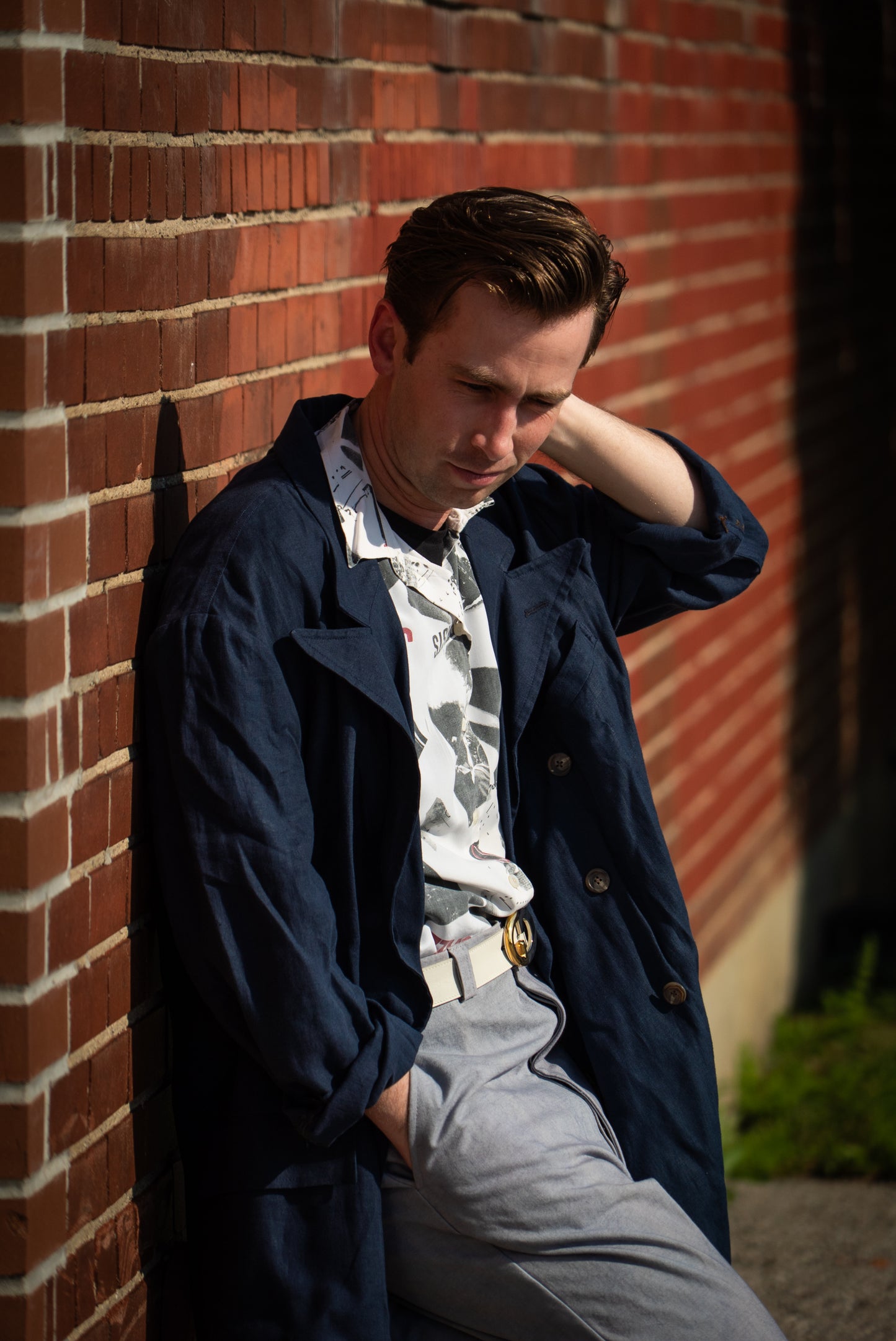 Man leaning against a brick wall wearing a navy jacket and gray pants.